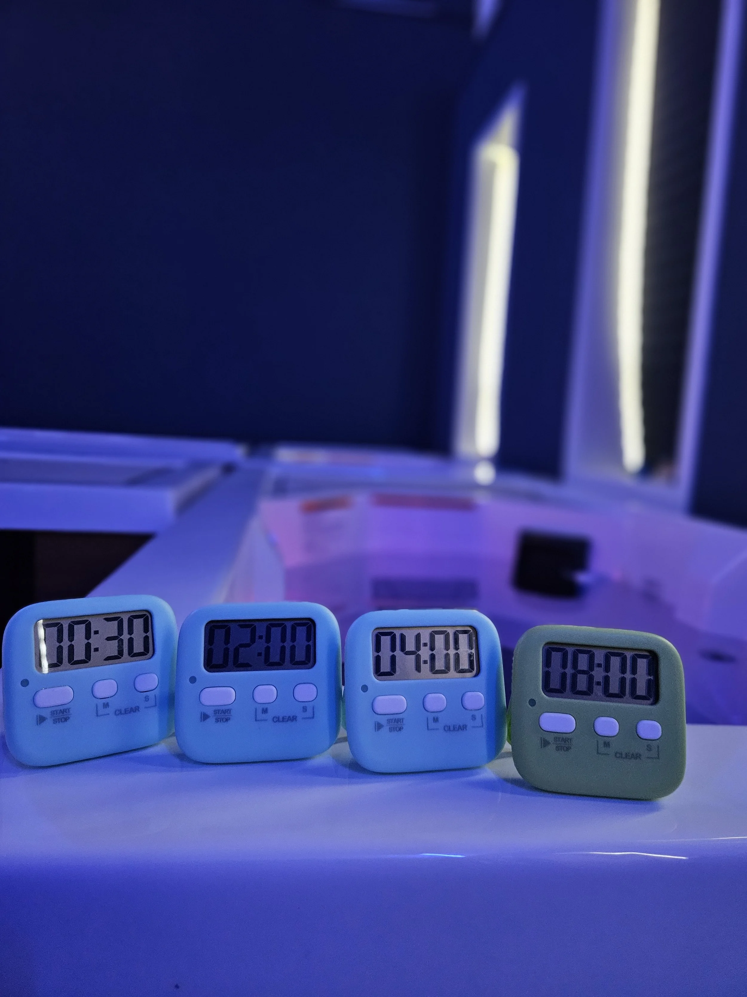 Four digital timers showing different times, placed on a flat surface, with a dark background and a blue tint lighting.