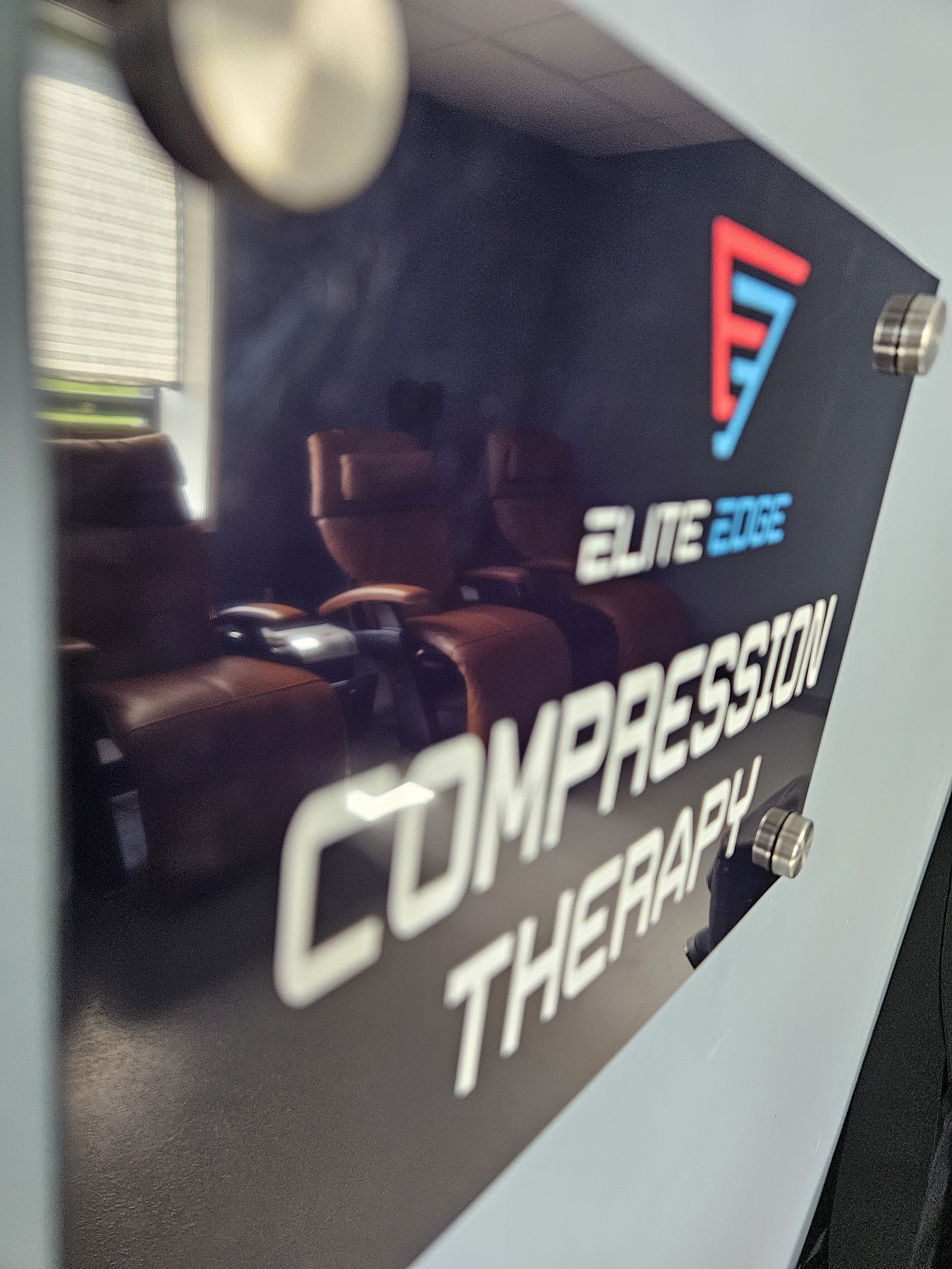 Close-up of a sign with the words "COMPRESSION" and "THERAPY" and the Elite Edge Recovery ogo with red and blue lines.