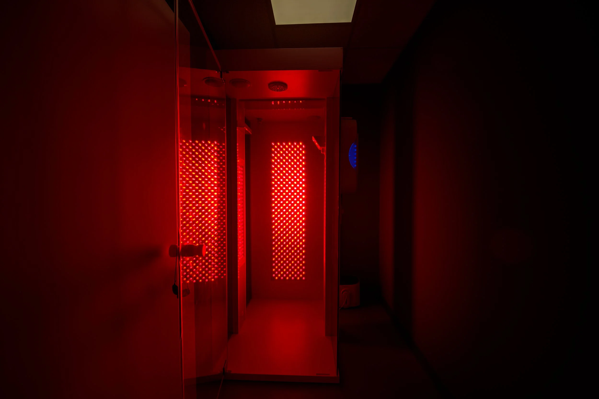 A red light therapy room with illuminated red panels on the walls and a mirror reflecting the panels.