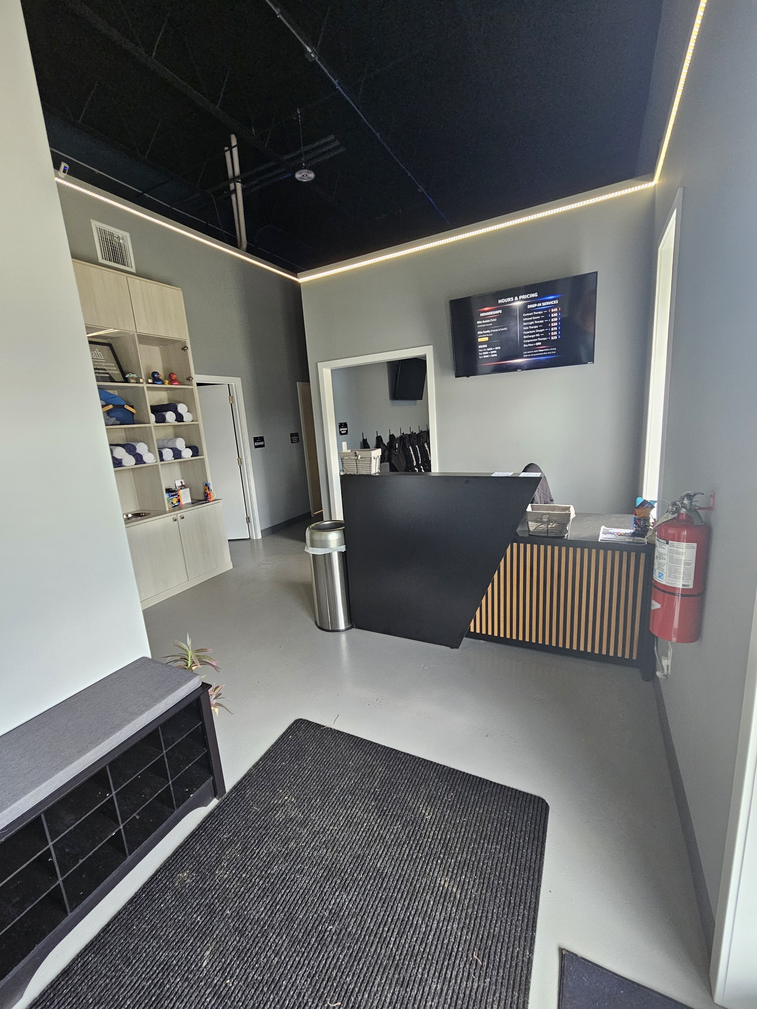 A Photo of the lobby of Elite Edge Recovery. There is a black desk, a tv with prices, a shoe rack, and a shelf with towels. A Premium Wellness center near you.
