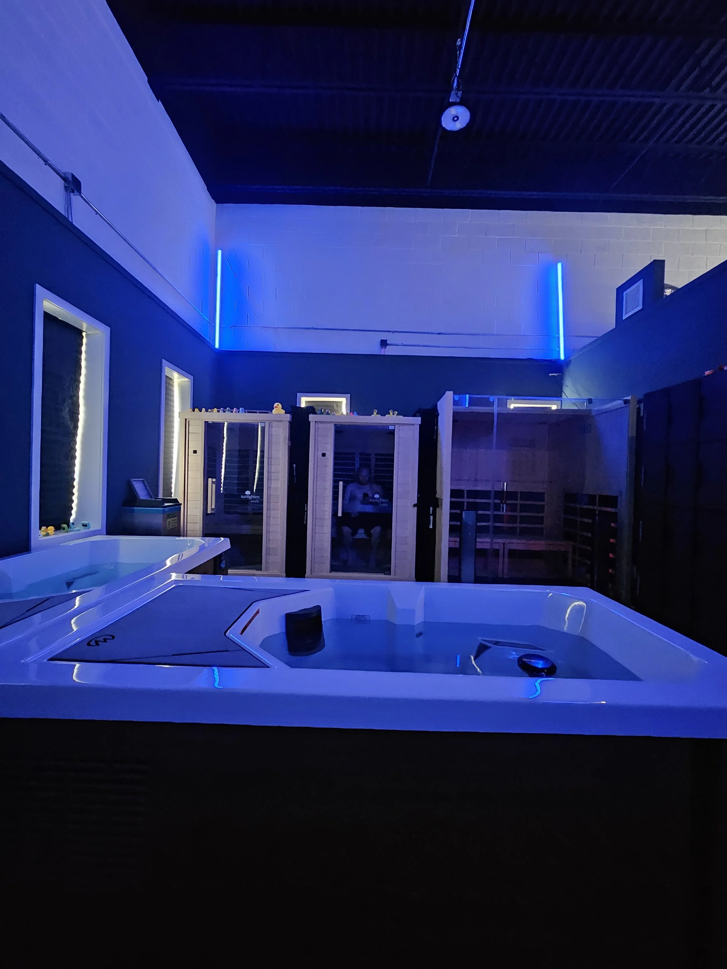 Indoor hot tub with blue LED lighting, wood sauna, and person sitting inside.