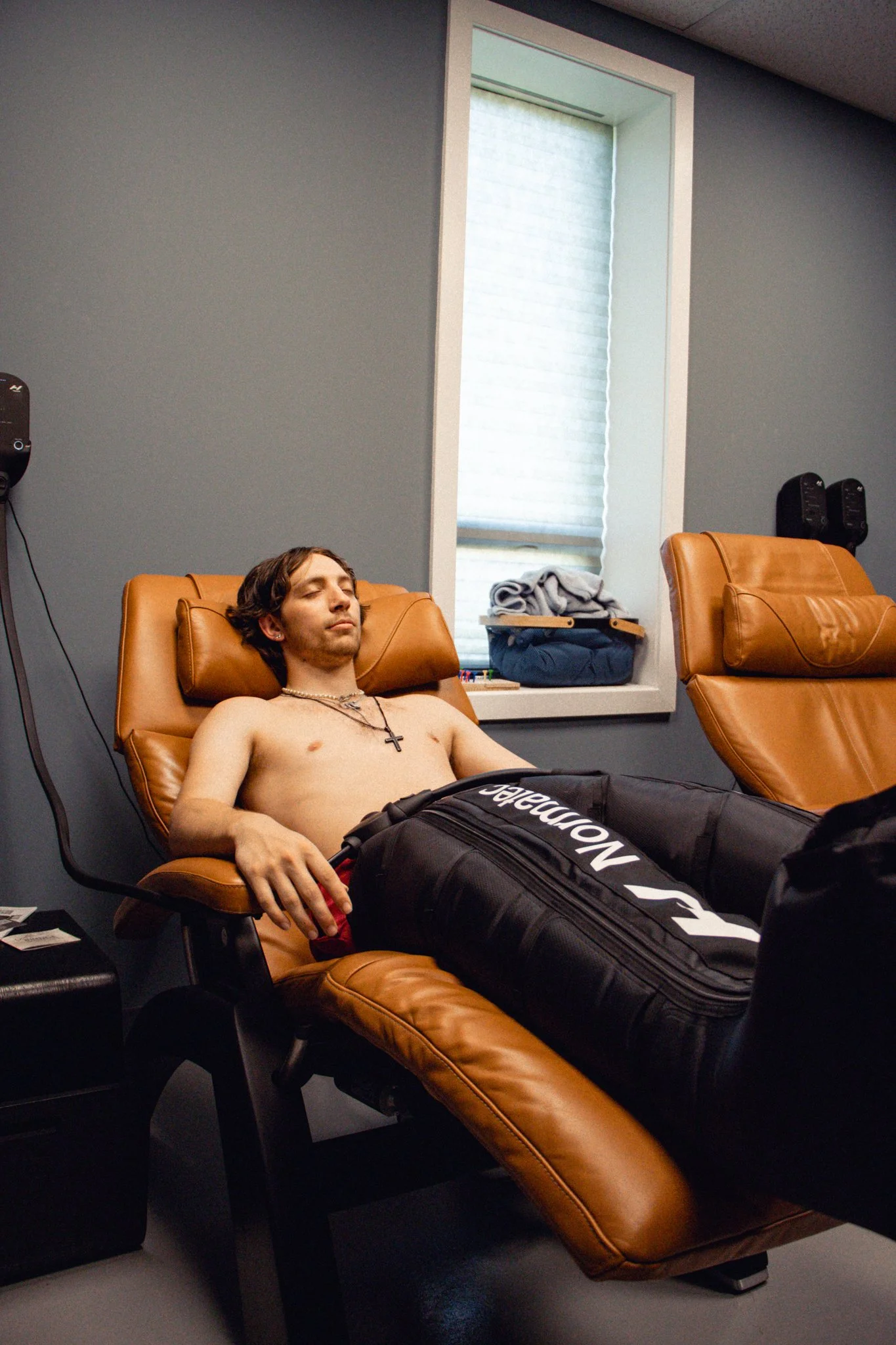 A young man sitting in a zero-gravity chair relaxing while using compression therapy boots in Lionville, PA