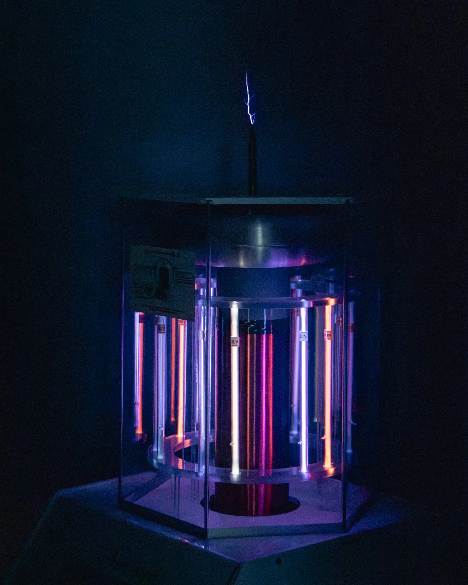 A Tesla coil glowing with purple and orange light, emitting visible electric sparks in a dark room.