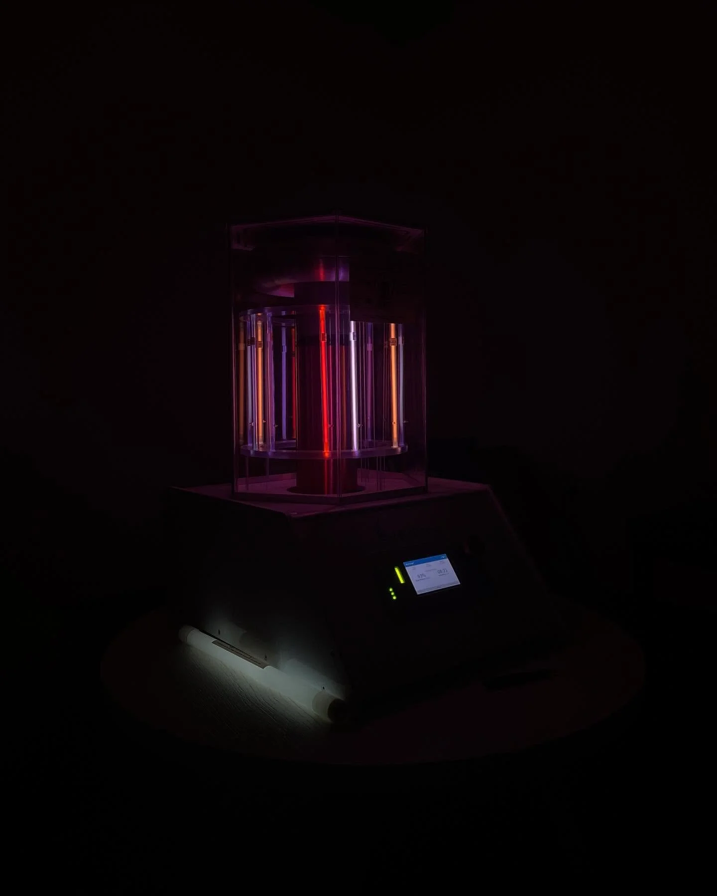 A scientific experiment device with illuminated neon lights inside a transparent enclosure, set against a dark background.
