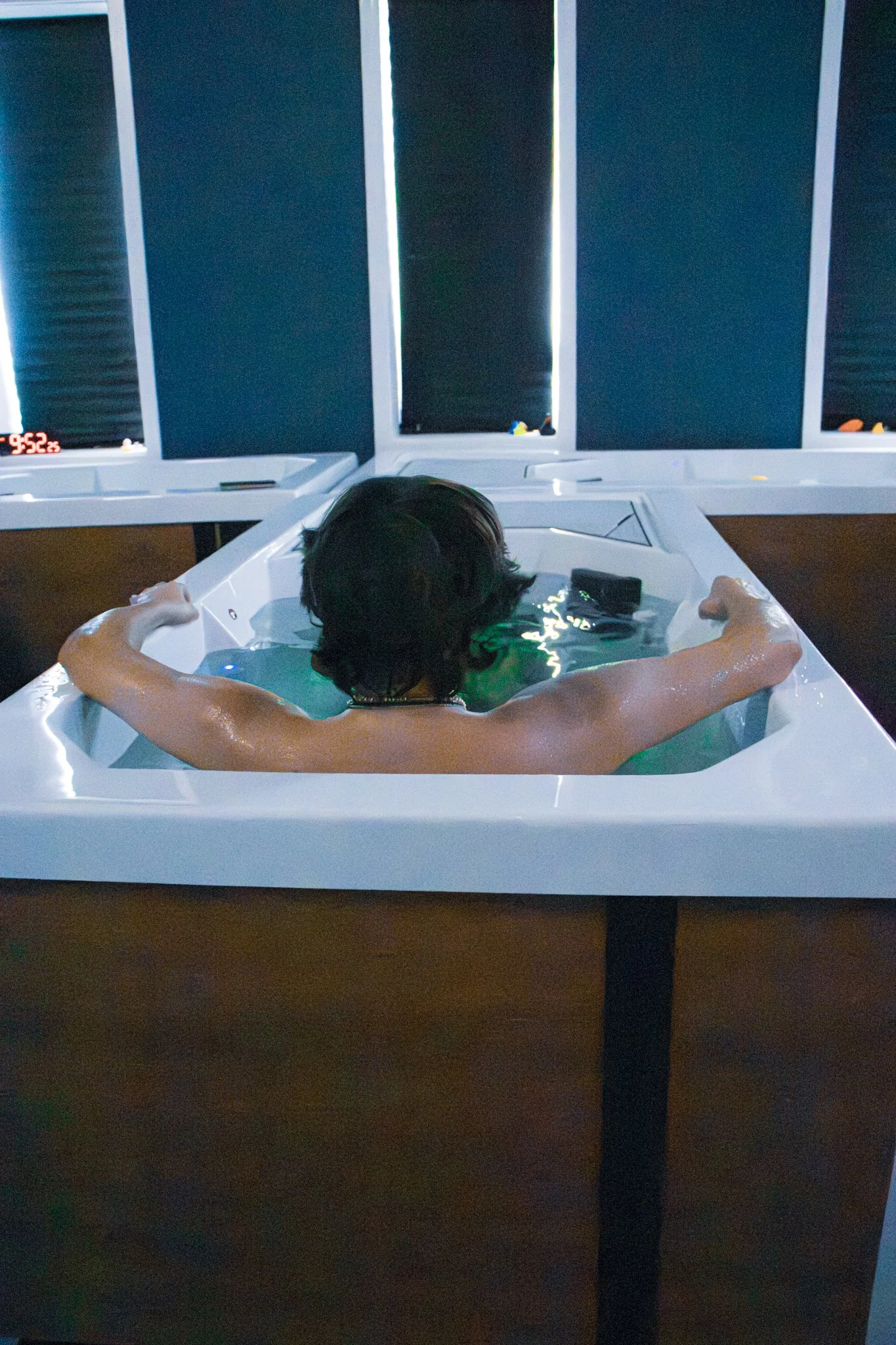 A man sitting in a hot tub relaxing while preforming Contrast Therapy. the background is blue with rubber ducks sitting near a window. it creates a calm, relaxing, and fun environment to recover.