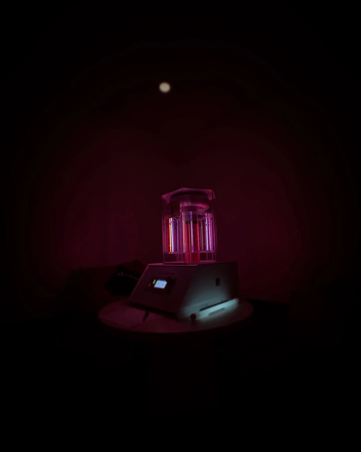 A BioCharger NG device emitting pink and purple light, electricity, frequencies, and PEMF in a dark room, with a small digital screen and control panel visible.