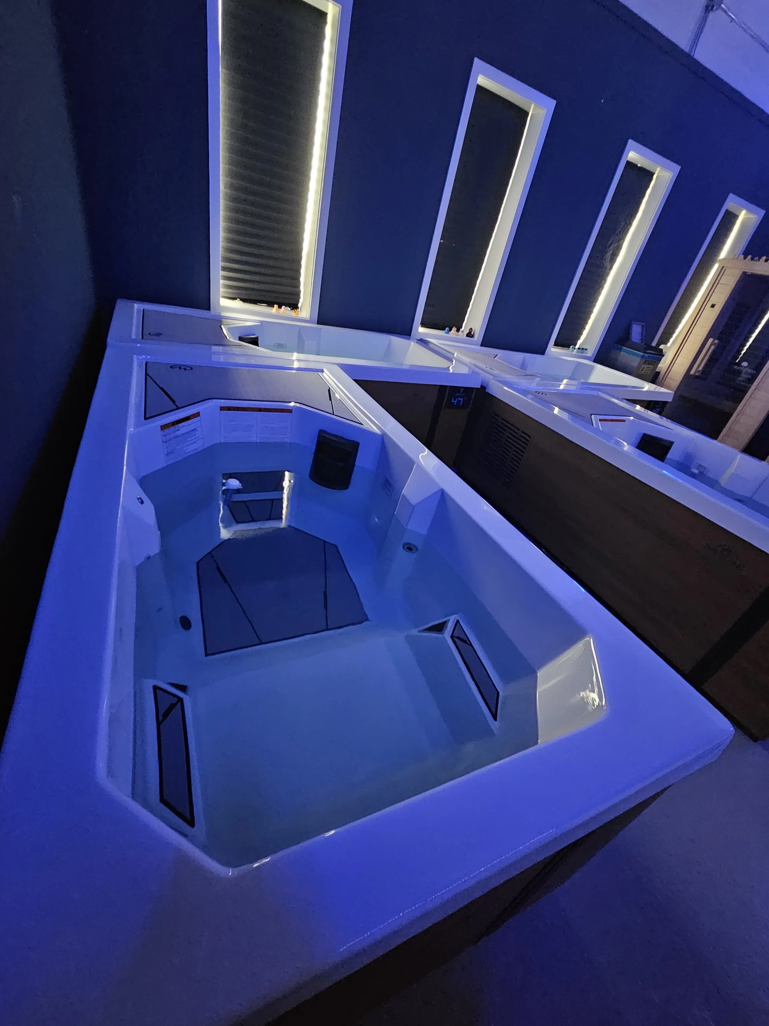 Empty hot tubs or jacuzzis in a room with blue lighting and vertical rectangular windows.