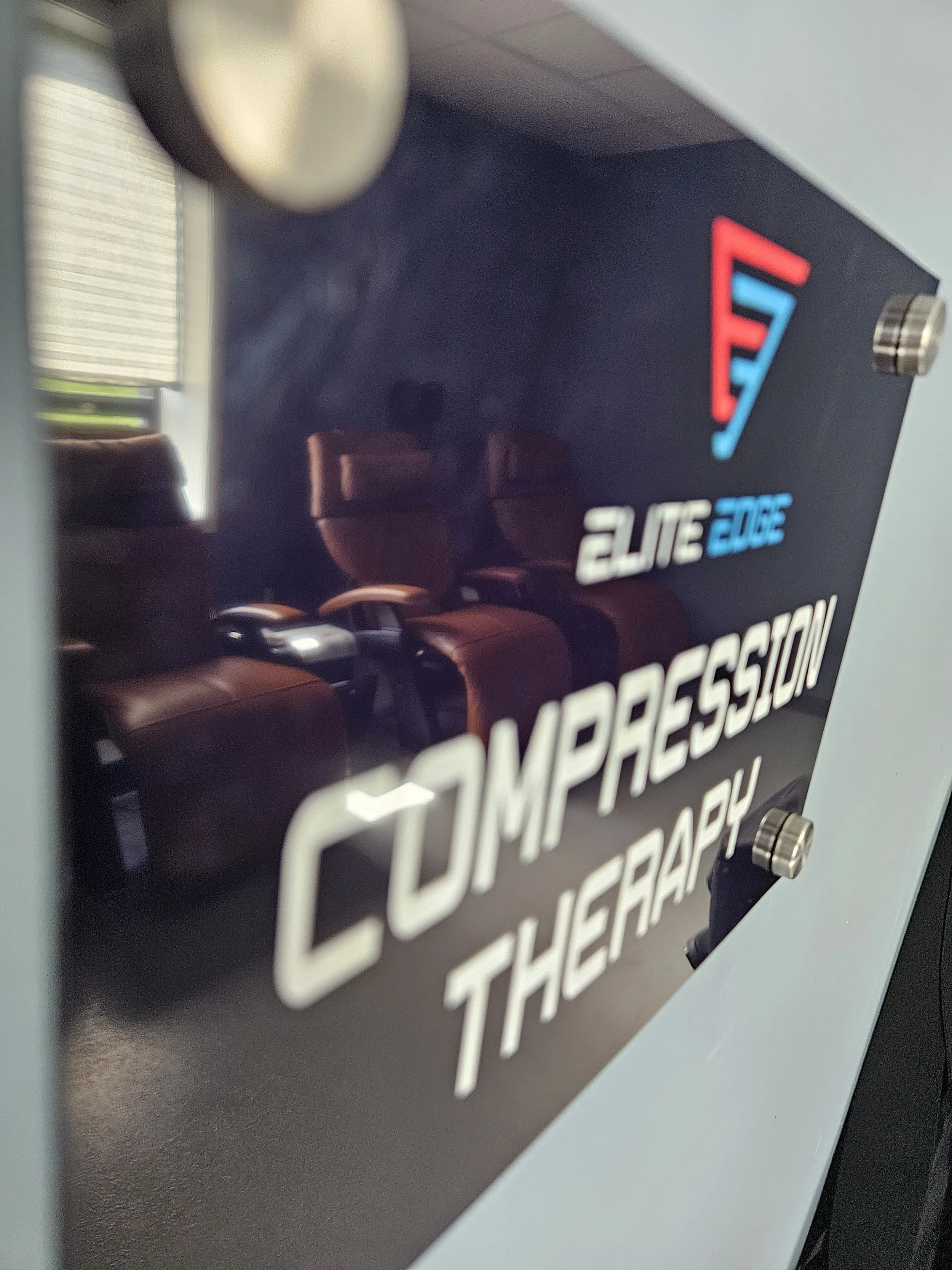 A sign with the Elite Edge logo, featuring a stylized red and blue triangle, reading 'Elite Edge' in white and blue text, and the words 'Compressor Therapy' in large white font.