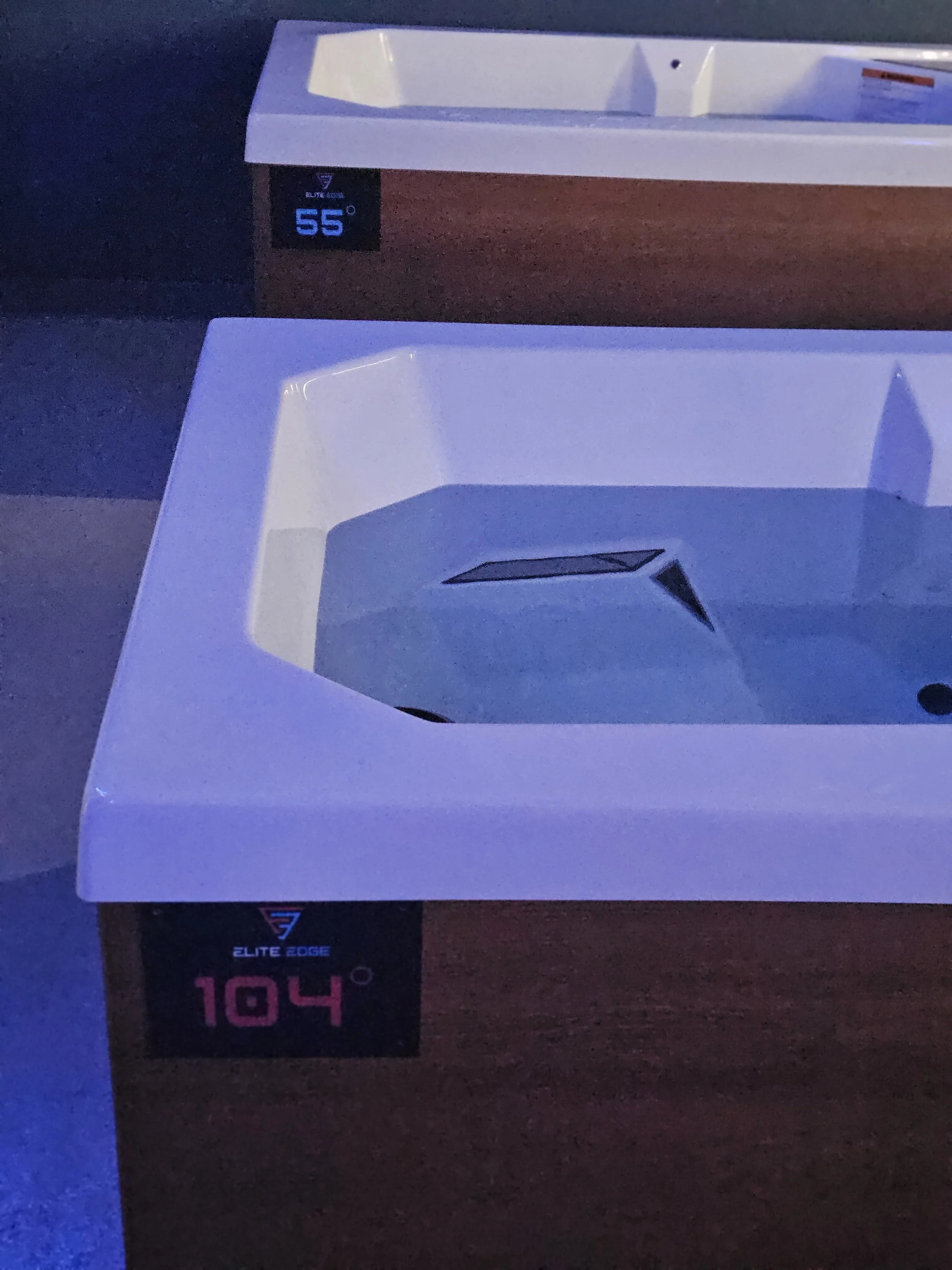 Two white rectangular bathroom sinks with digital temperature displays underneath each, showing 55 and 104 degrees, on a wooden countertop.