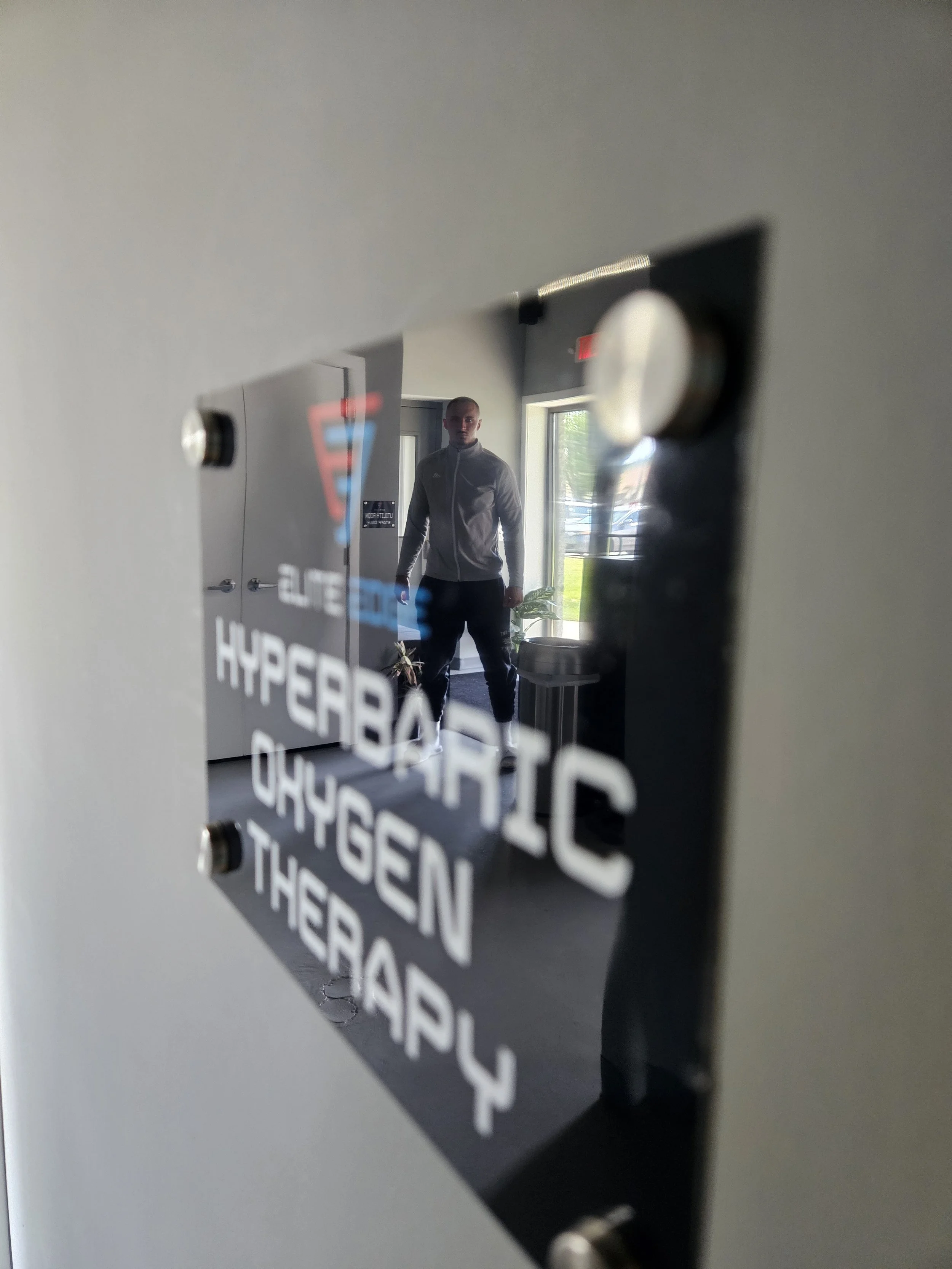 A sign that reads "hyperbaric oxygen therapy" and in its reflection is a man who is a professional fighter in UFC, MMA, and Boxing.