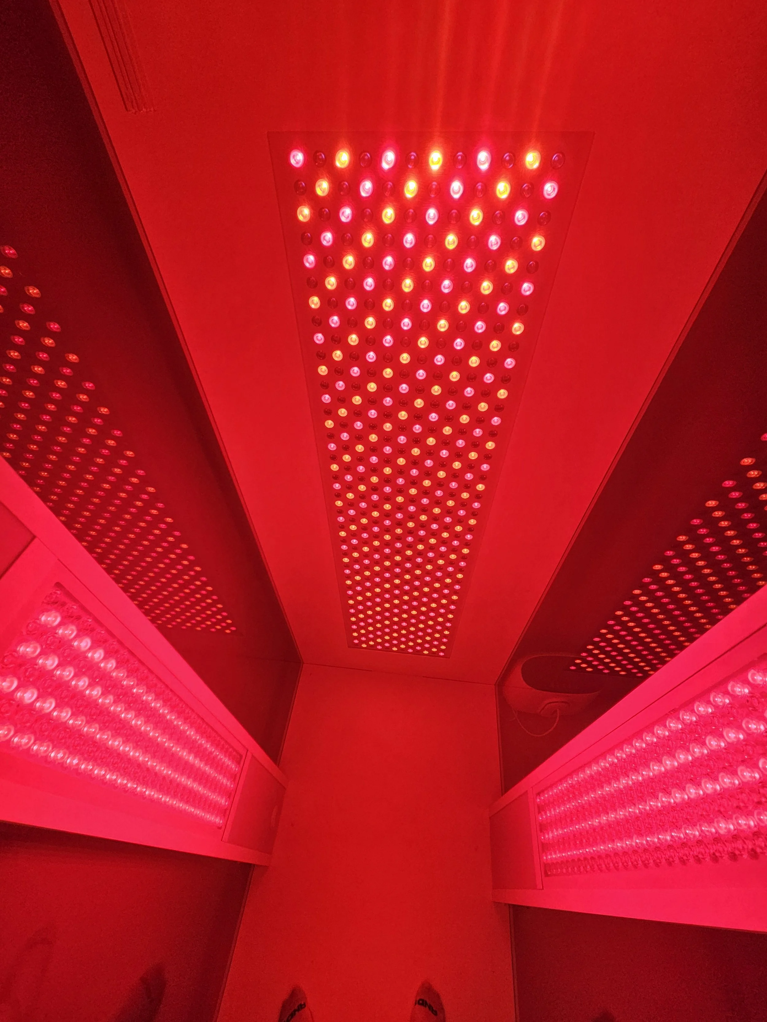 Red LED light therapy panels on ceiling and walls of a small room or enclosure, emitting bright red light.