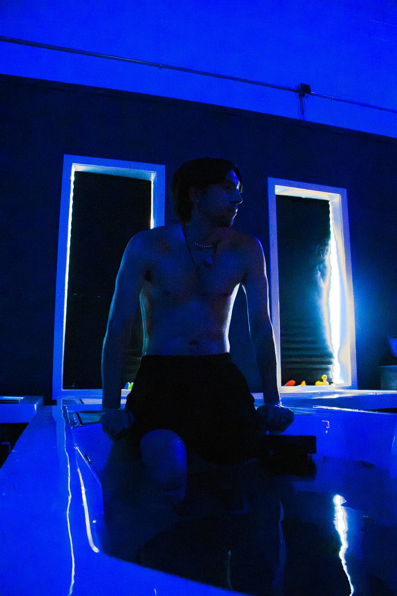 A Young man sitting on the edge of a cold plunge in a blue lit room at Elite Edge Recovery in Malvern, PA.