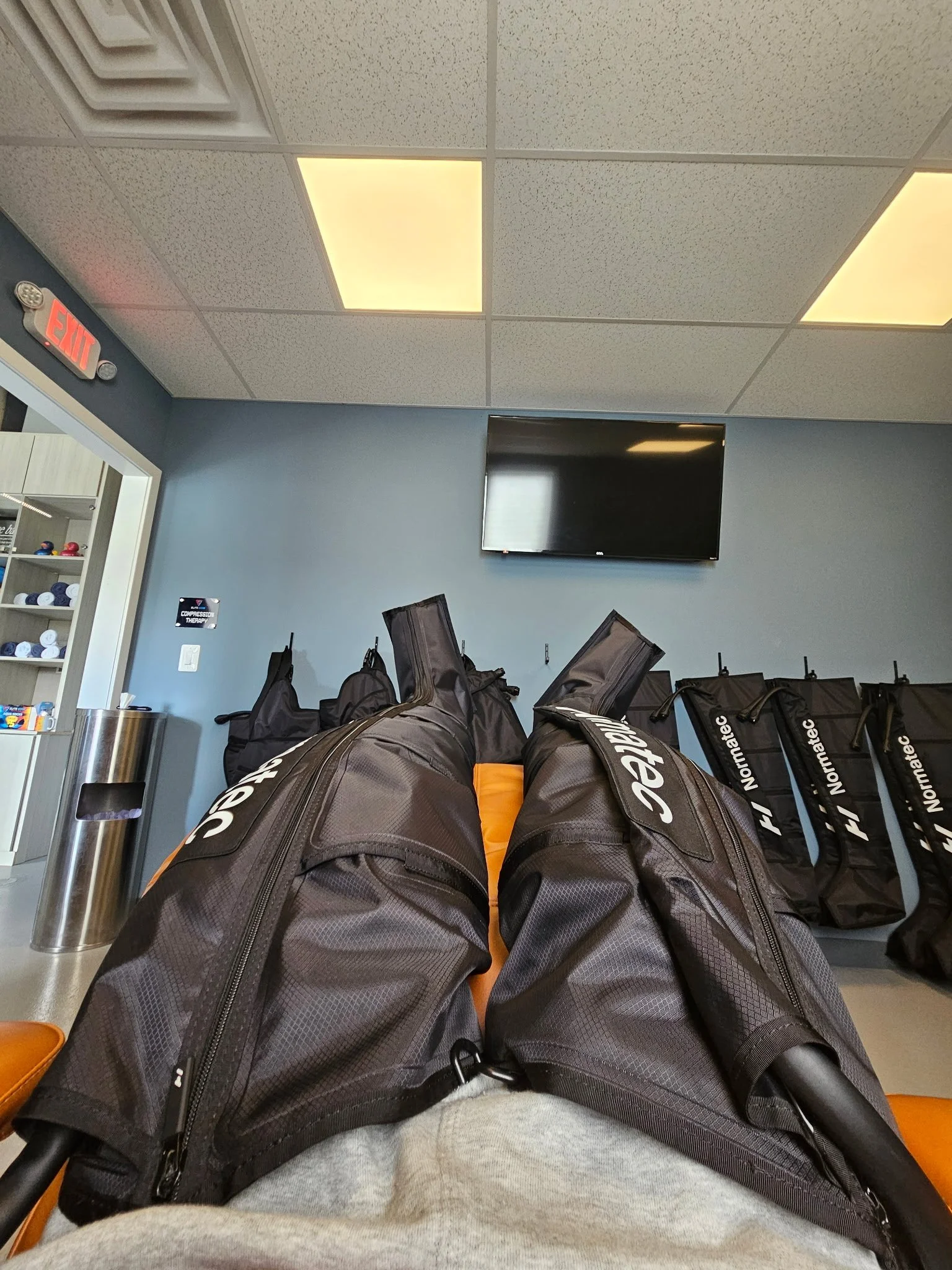 View from a person's perspective lying on a bench with four golf bags, in a waiting area of a golf facility.