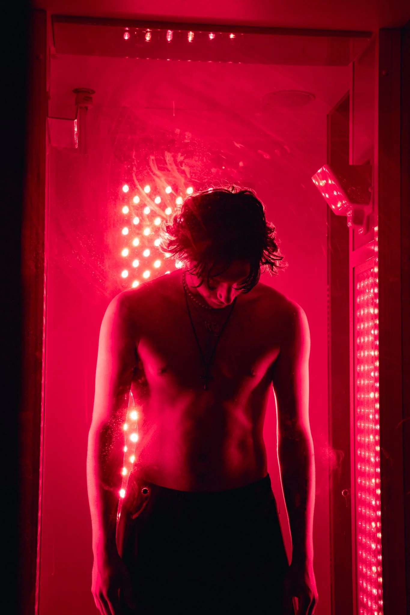 A young man in a red-light therapy booth looking down at his feet in Malvern, PA..