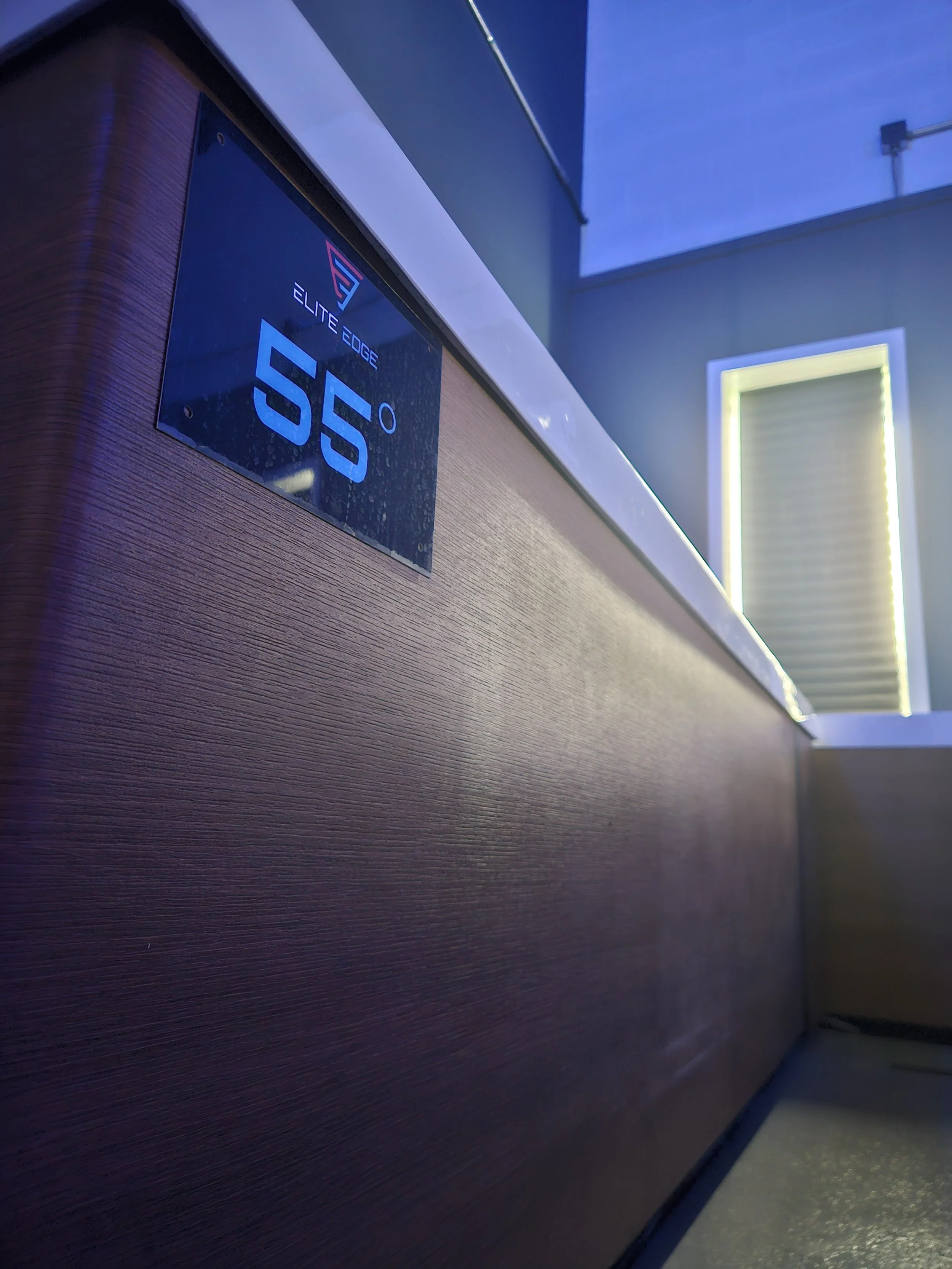 Close-up of an electronic temperature control panel displaying 55 degrees, mounted on a wooden surface, with a modern interior background.