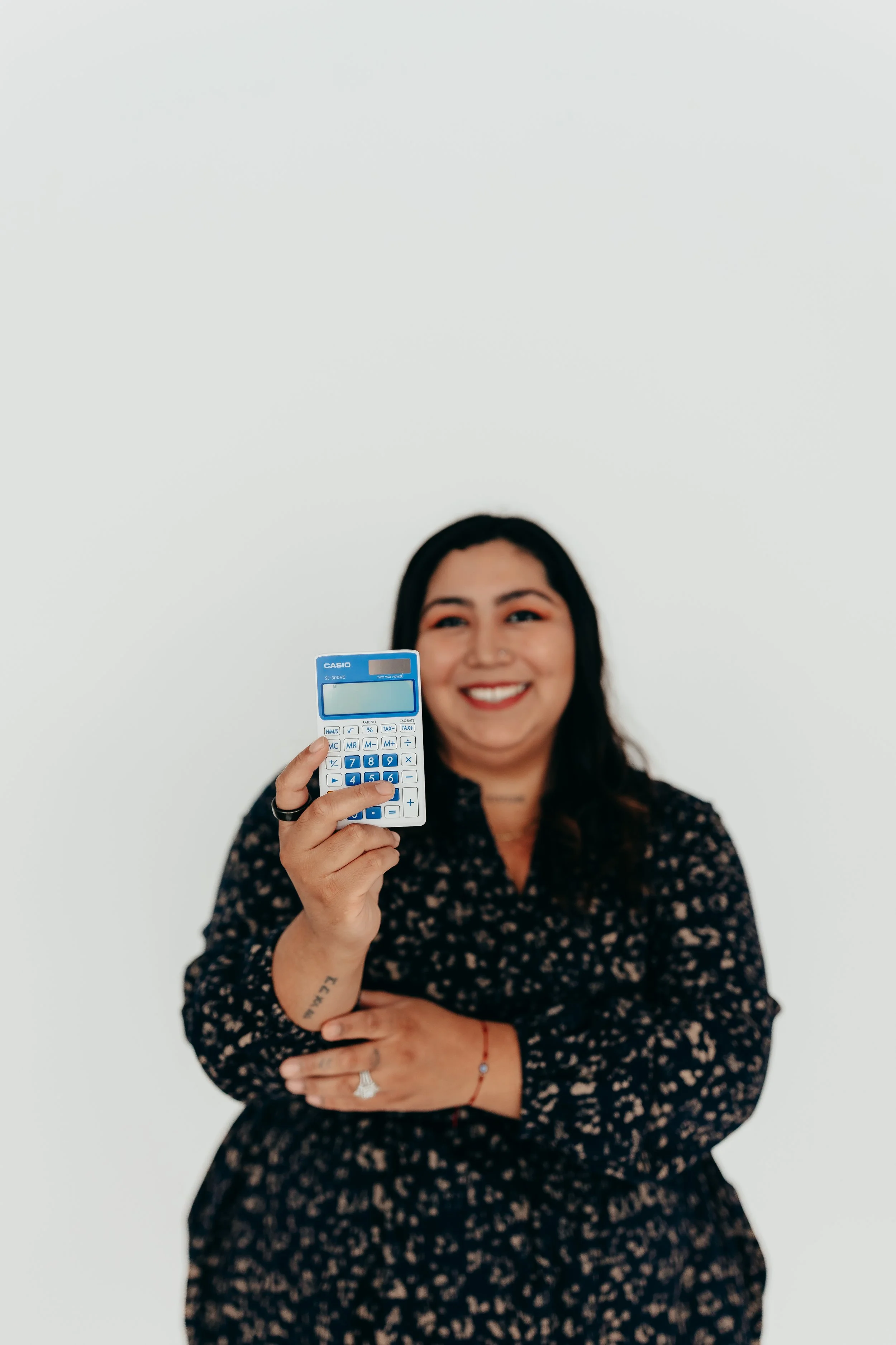 Smiling woman in a dark floral blouse holds a blue Casio calculator in front of a white background.