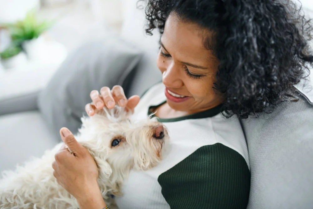 A woman cuddling a small white dog while sitting on a couch at home