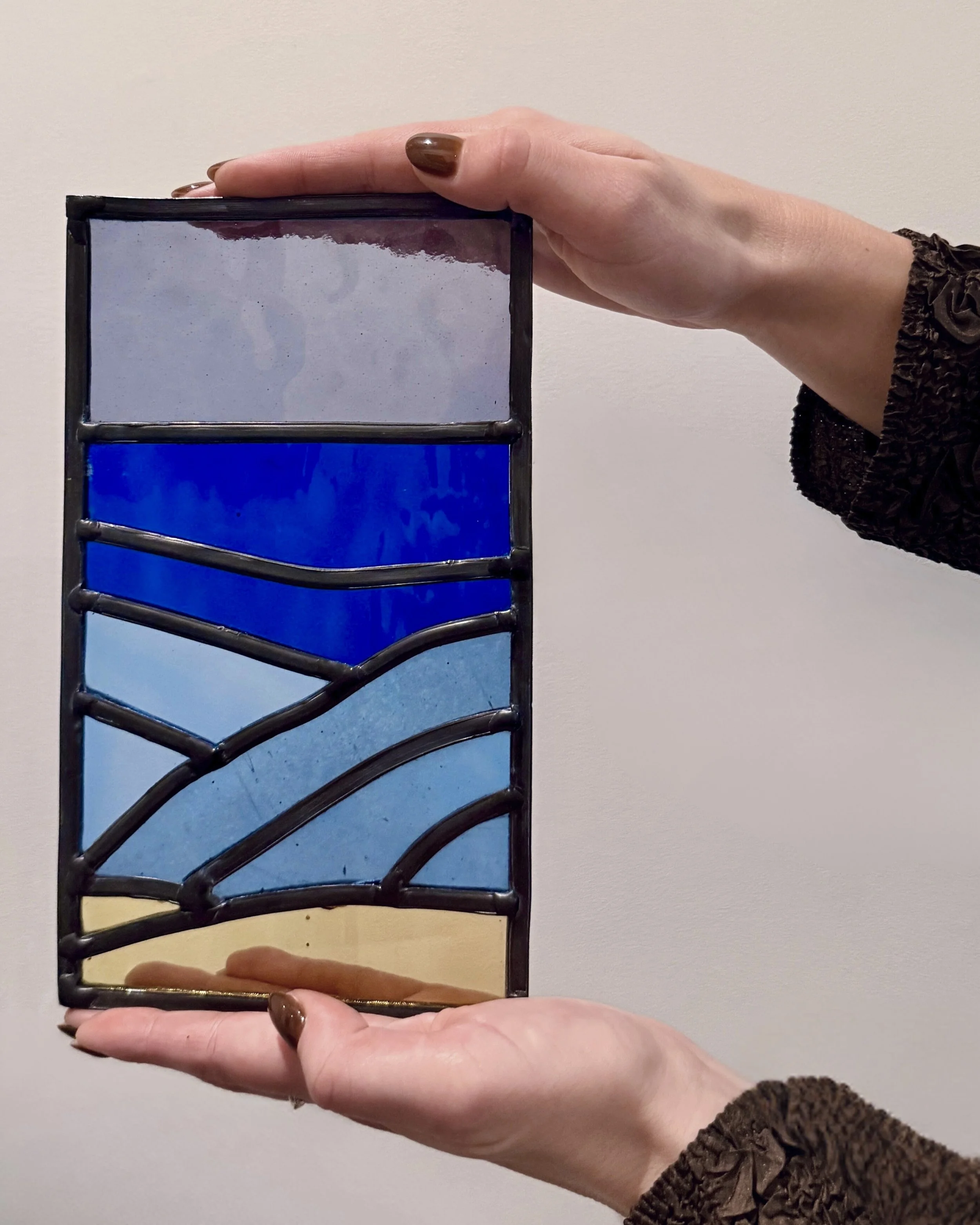 Een hand houdt een klein glas in lood raam met een ontwerp van het strand met de zee.