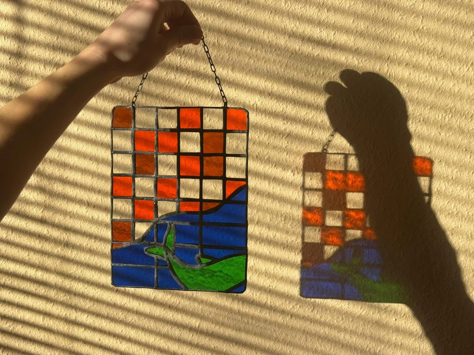 Een abstract glas in lood raam met een dolfijn in zee en een geblokte achtergrond. 