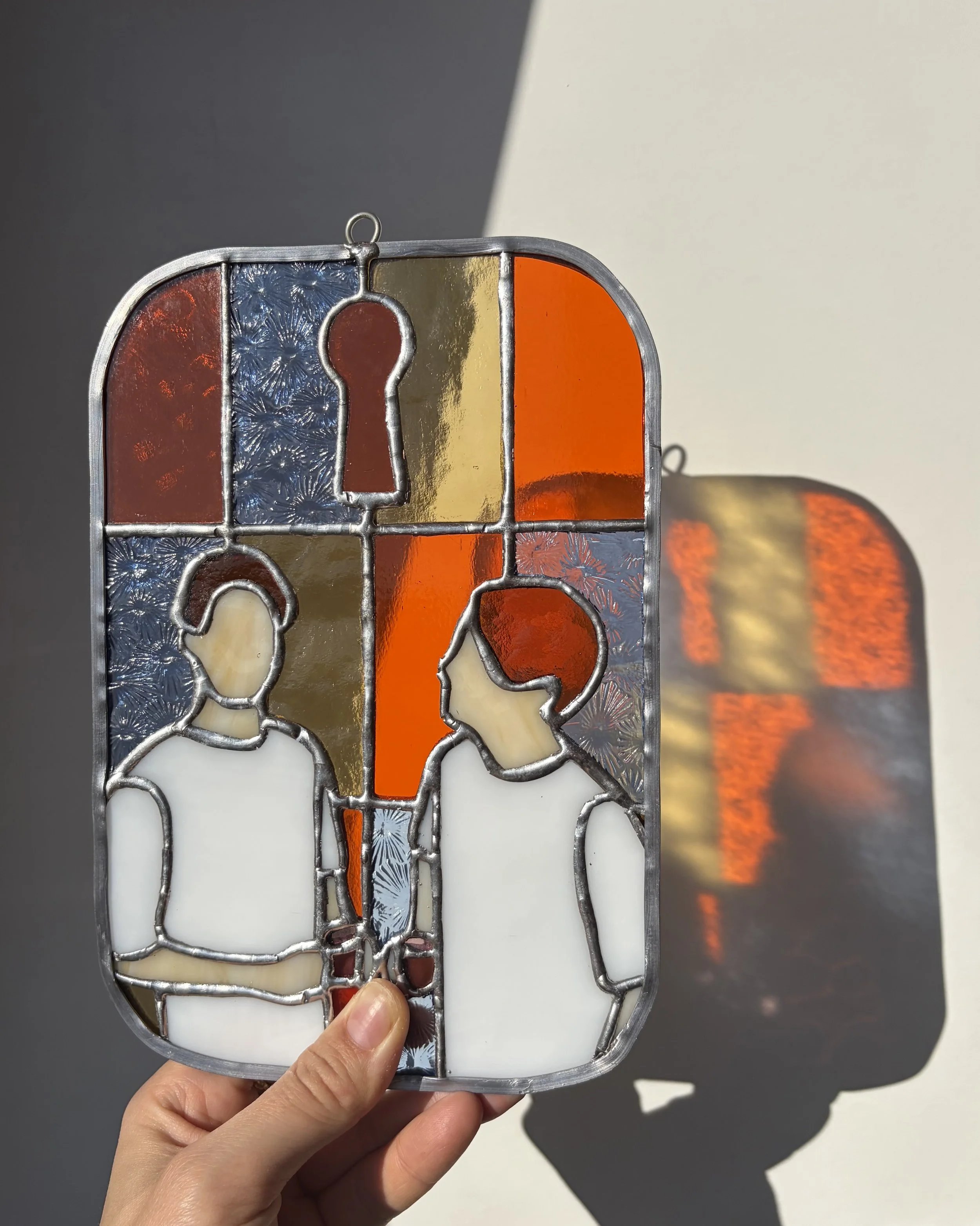 Glas in lood raampje van twee figuren tegen een geblokte achtergrond.