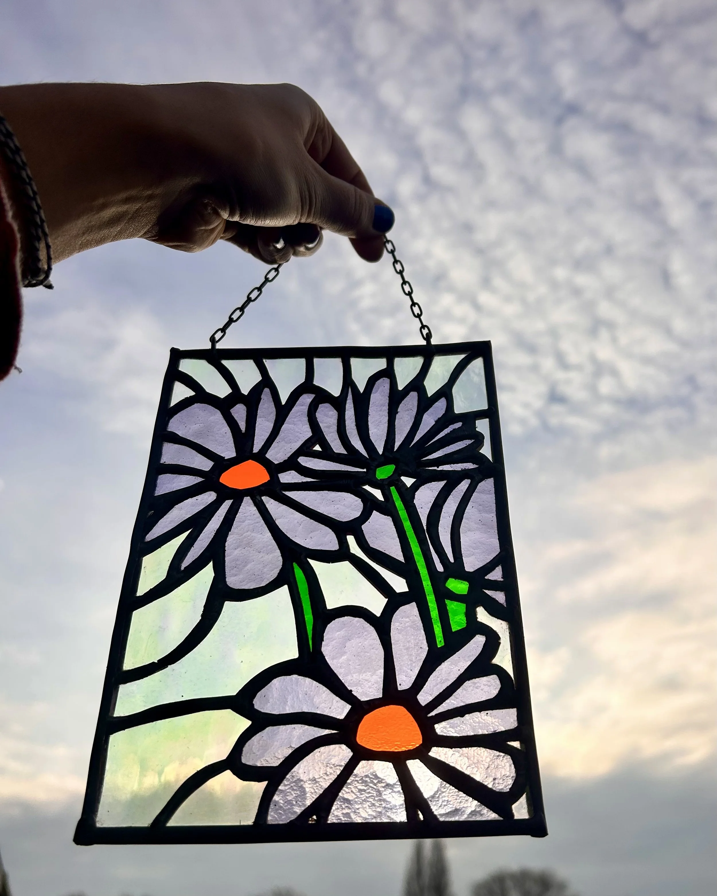 Een kunstwerk met gekleurd glas in een metalen frame in de vorm van bloemen, tegen een bewolkte hemel.