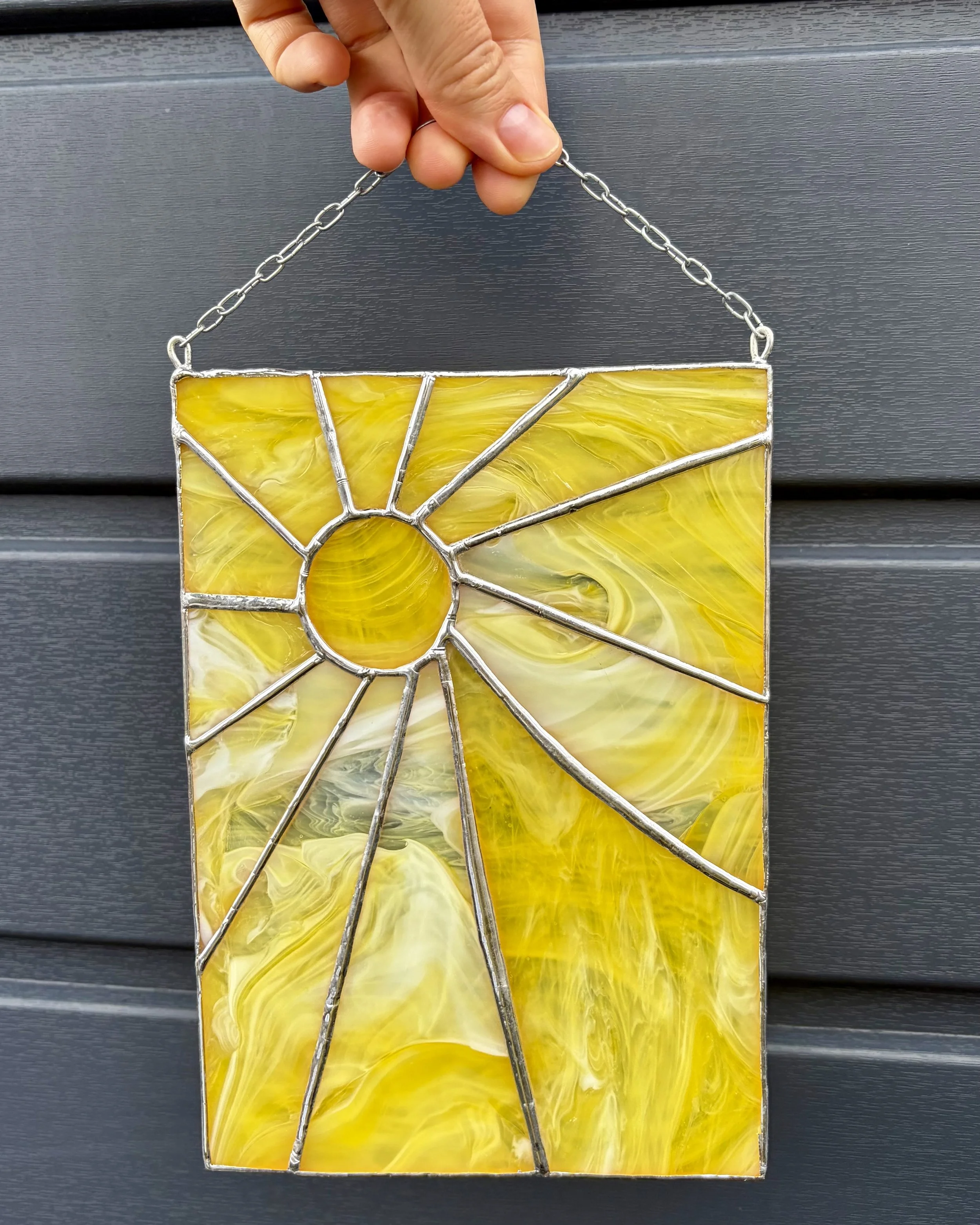 Man houdt een glas in lood werk vast met het ontwerp van de zon en geel glas.