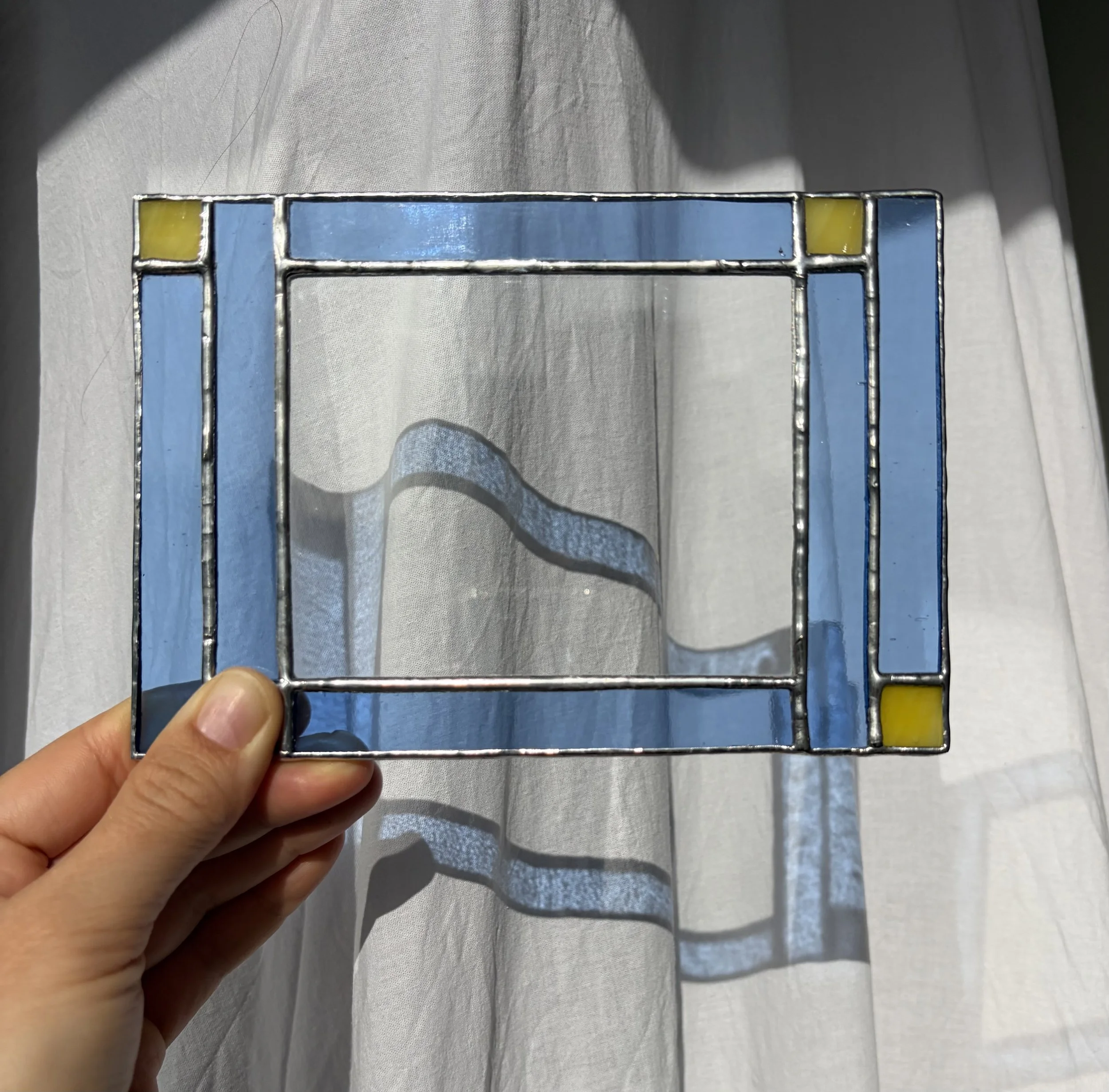 Hand houdt een gesneden stuk van een glas-in-lood raam met blauw en geel glas op een witte achtergrond.