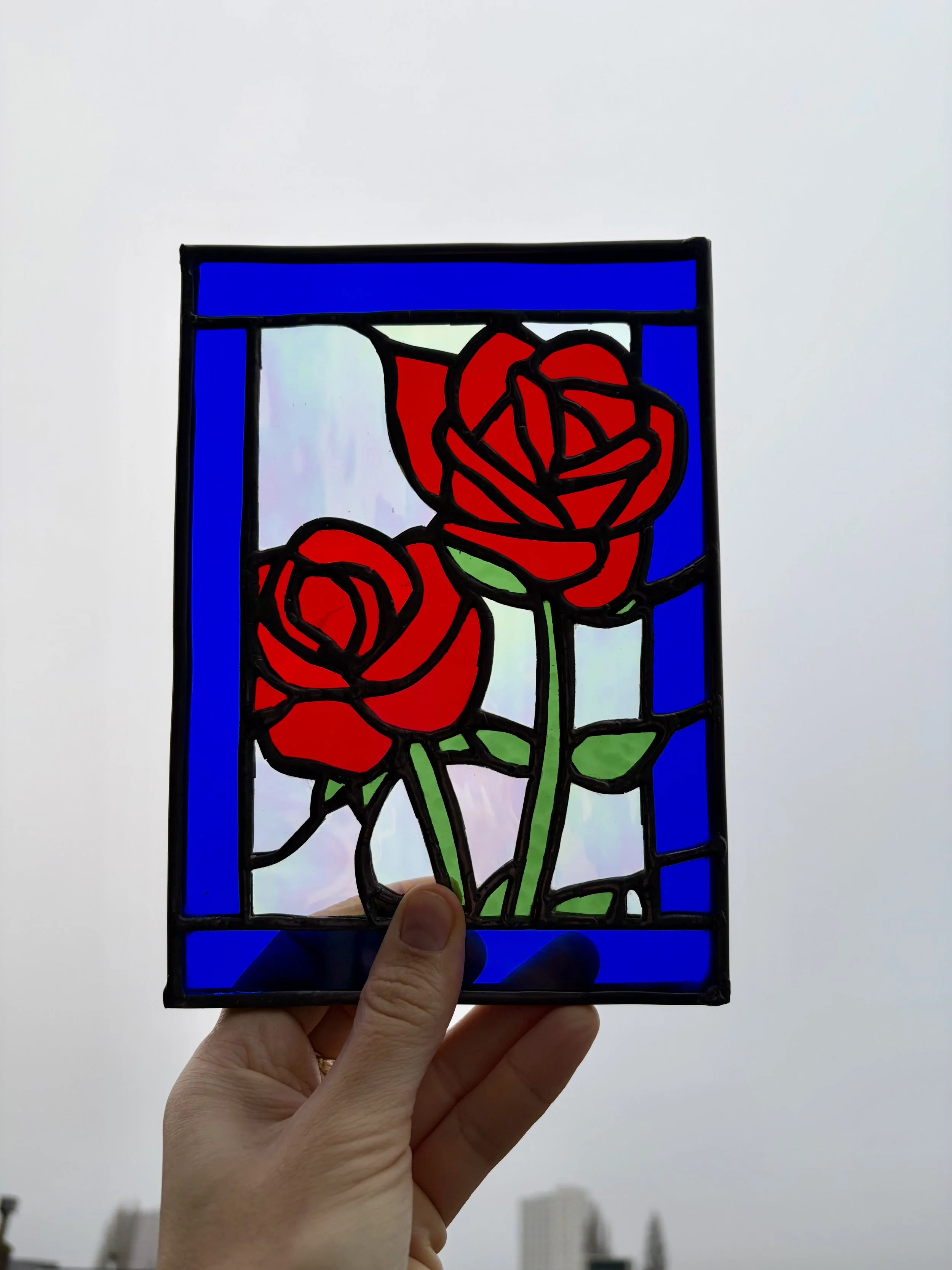 Een glas in lood raam met rode rozen en goede bladeren wordt in de lucht vastgehouden. 