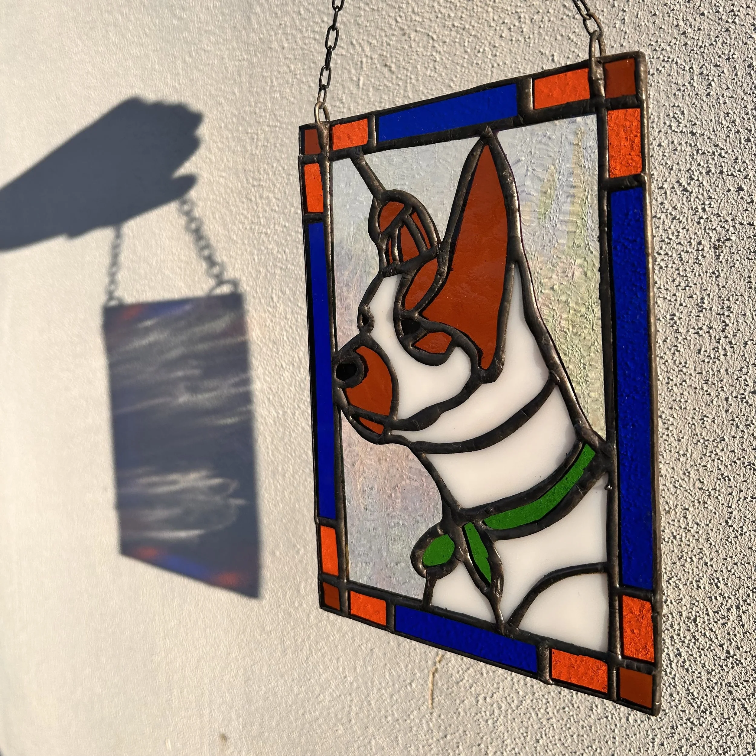 Een gestileerde glazen wand met een hondsilhouet in zwart met oranje en groene details, bevestigd aan een muur.