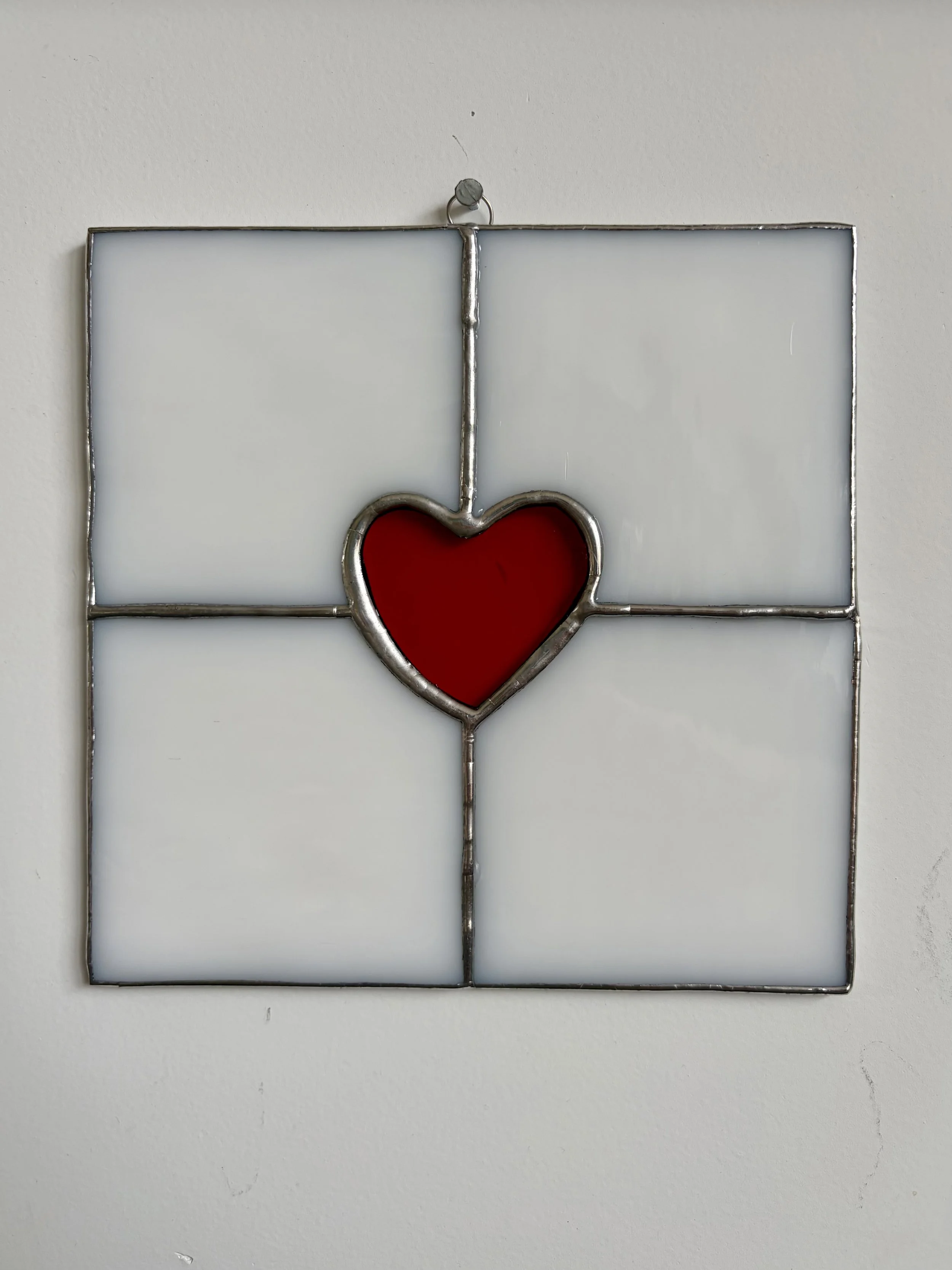 Glasraam met een rood hartvormig patroon in het midden, bevestigd aan een witte muur.