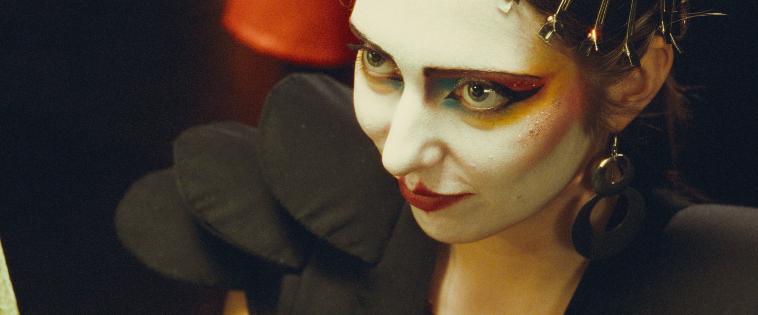 Nahaufnahme einer Frau mit ausgefallenem Make-up, schwarzen Lederhandschuhen und bunten Haarwicklern, im Stil der 1980er Jahre.