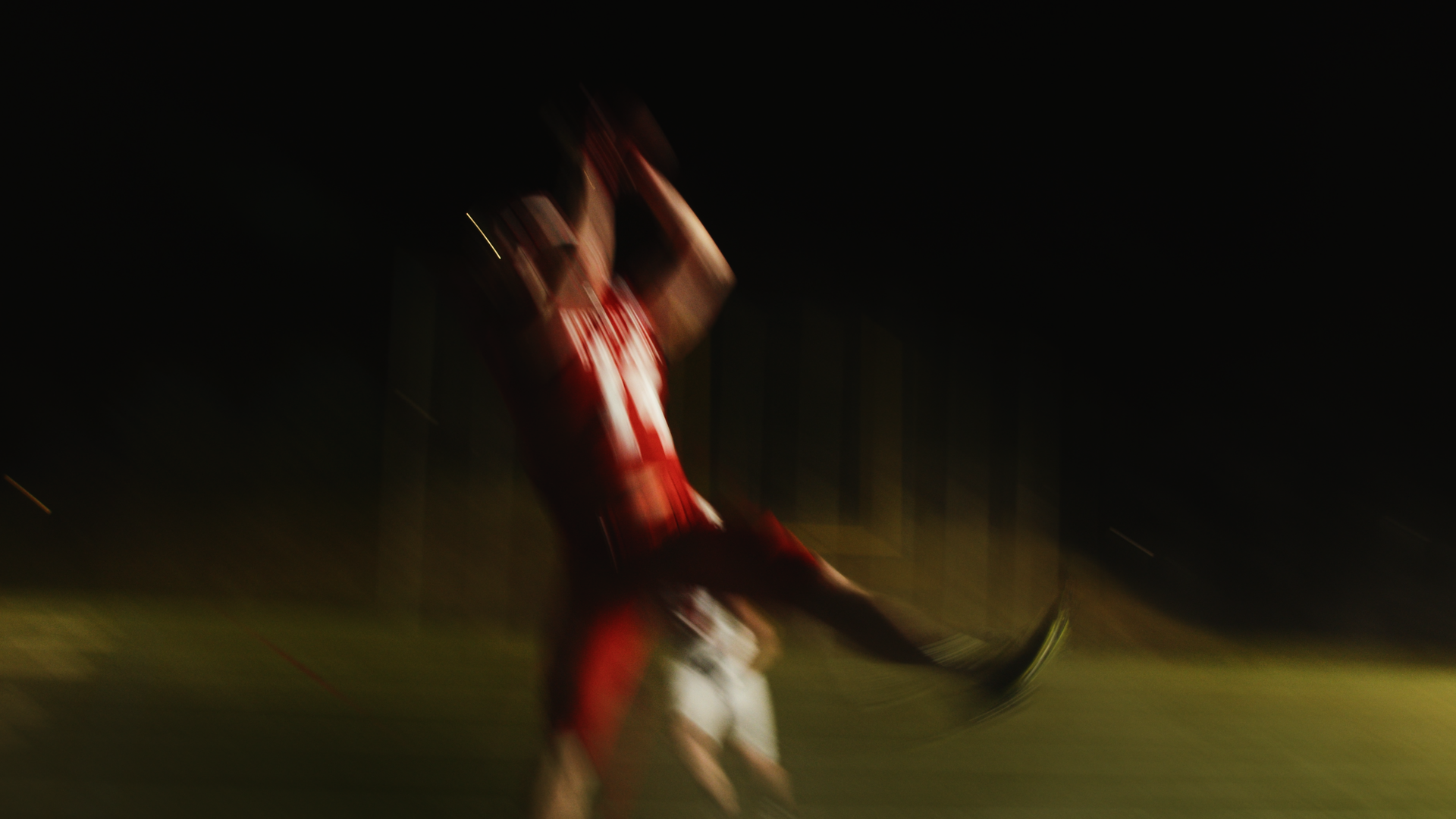 Bewegtes Bild eines Mannes in rotem Trikot, der auf einem Sportfeld bei Nacht spielt.