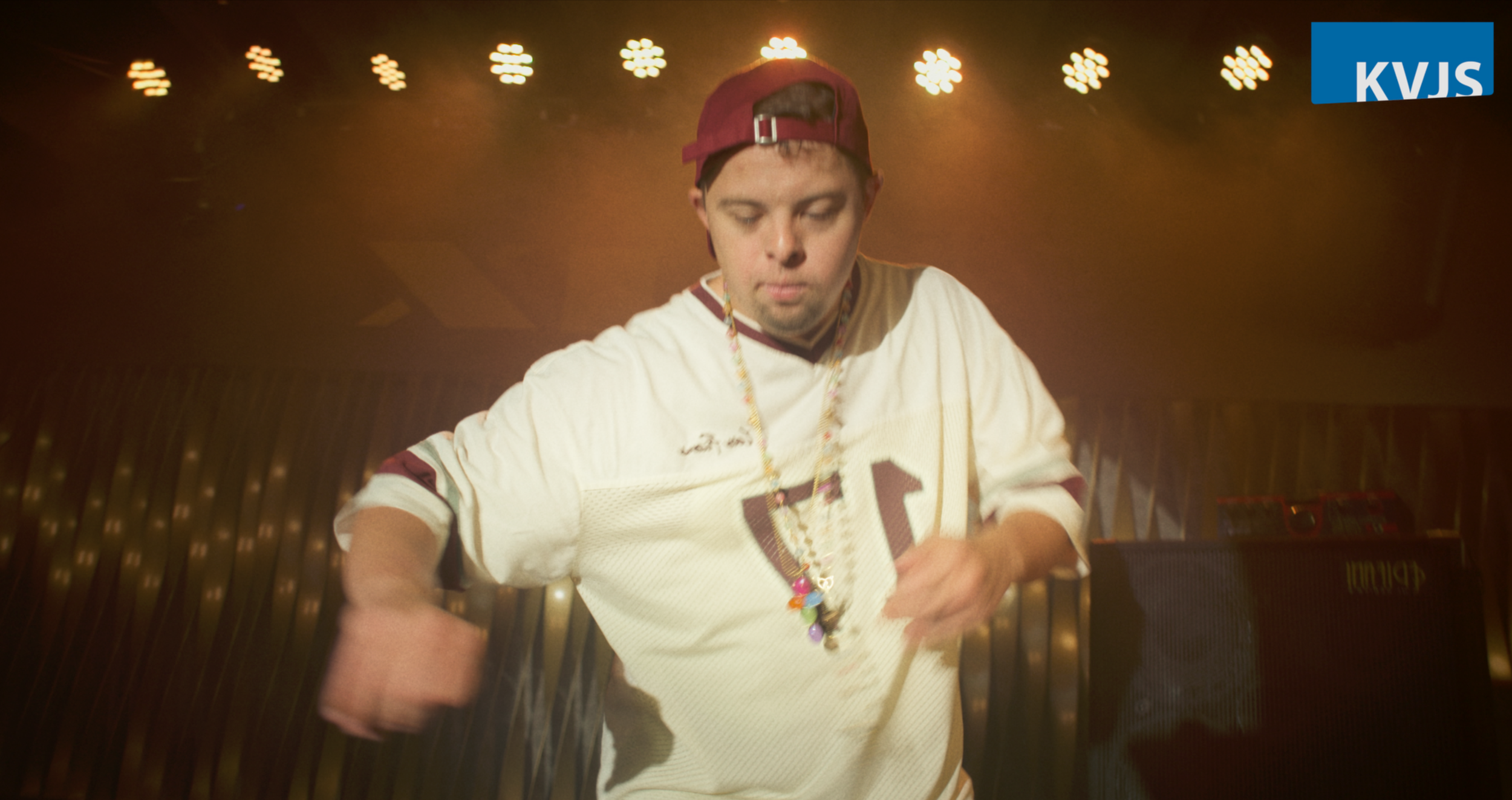 Junge männliche Person mit Baseballkappe, Schmuck und Trikot beim Musikauftritt auf der Bühne