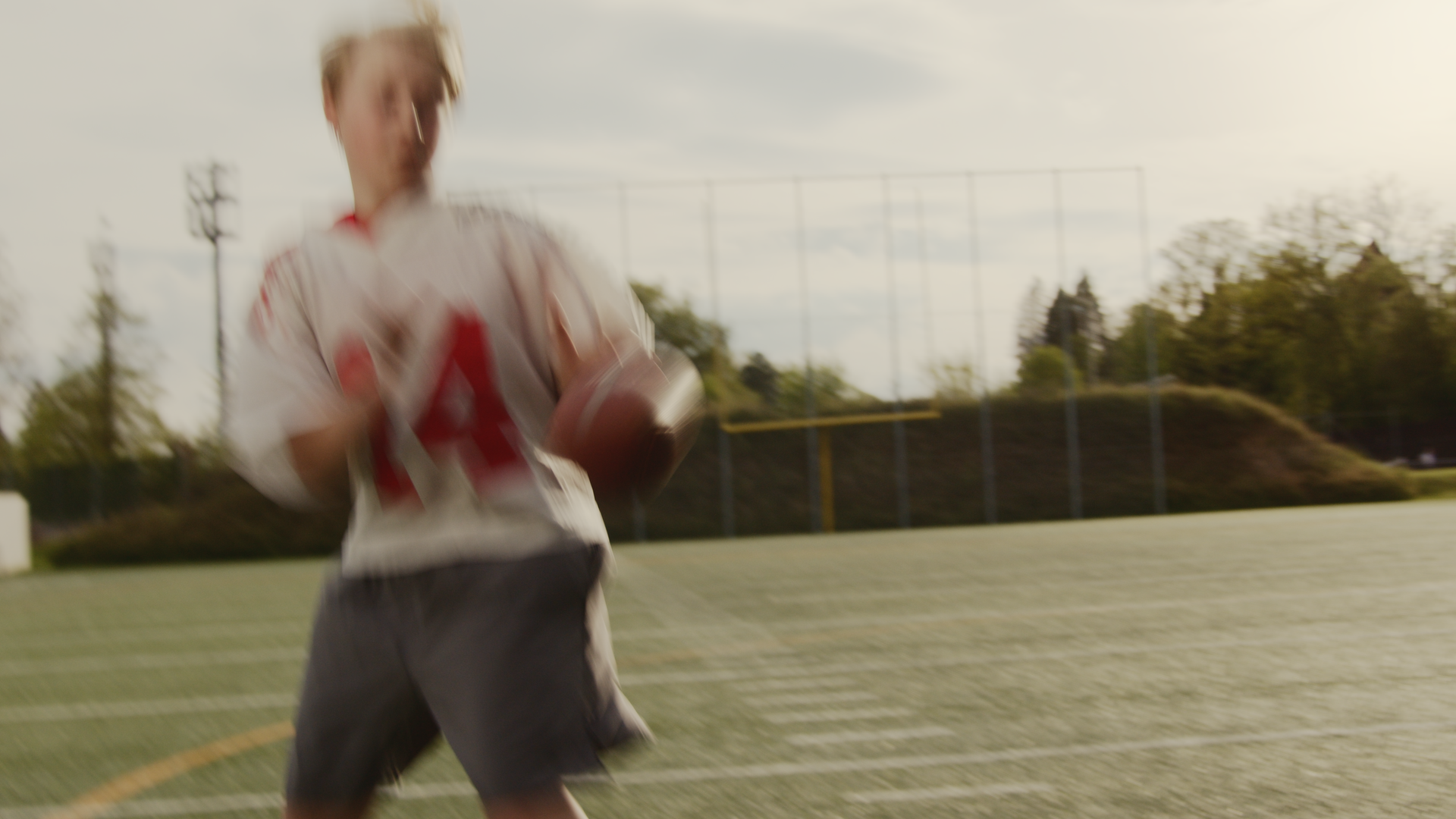 Ein junger Mann spielt American Football auf einem Sportfeld, trägt ein Trikot mit einer roten Nummer 4 und läuft.