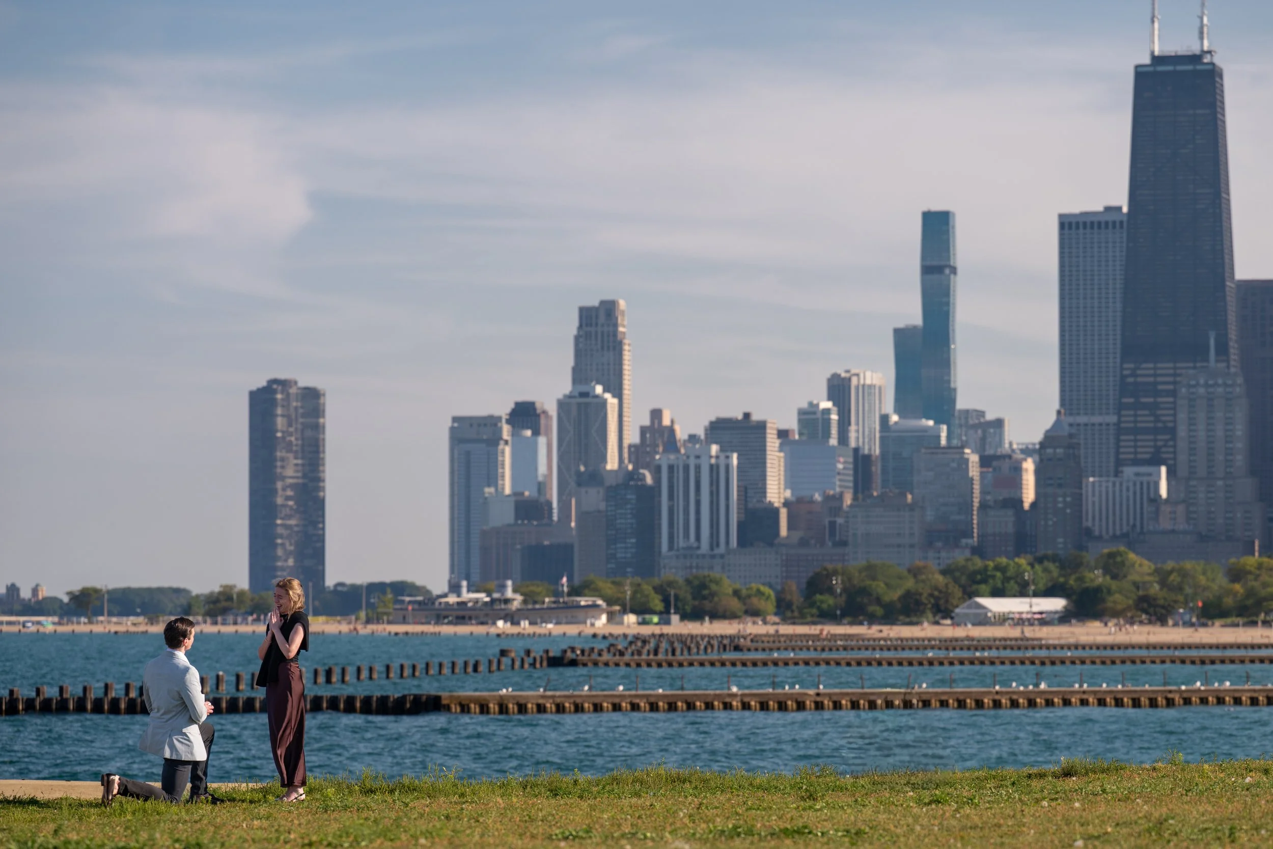 A couple proposing by the water with the Chicago skyline in the background, including the tallest building, Willis Tower.