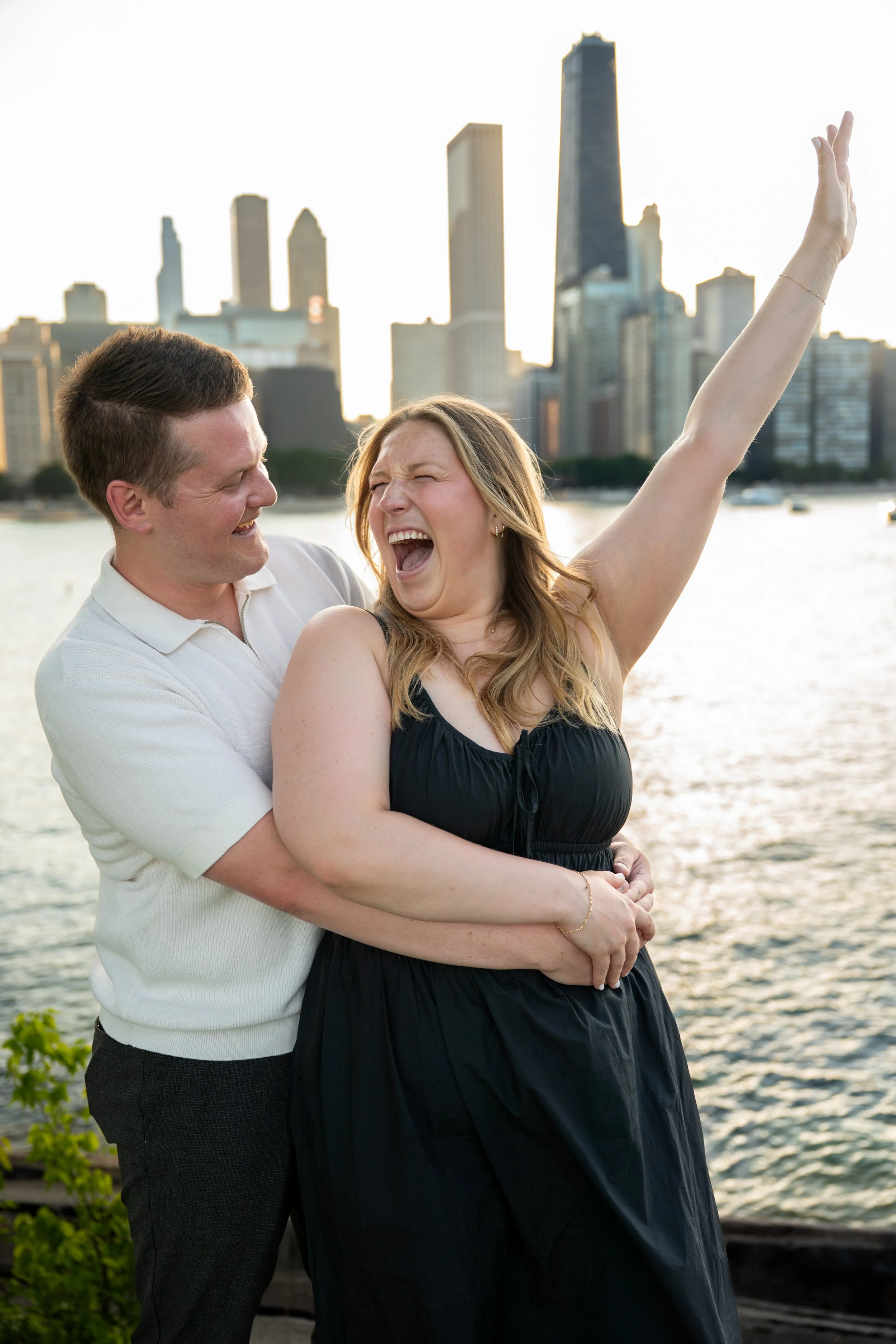 Photography of a couple enjoying a moment by the water with the Chicago skyline in the background, celebrating with expressions of happiness and love, during sunset.