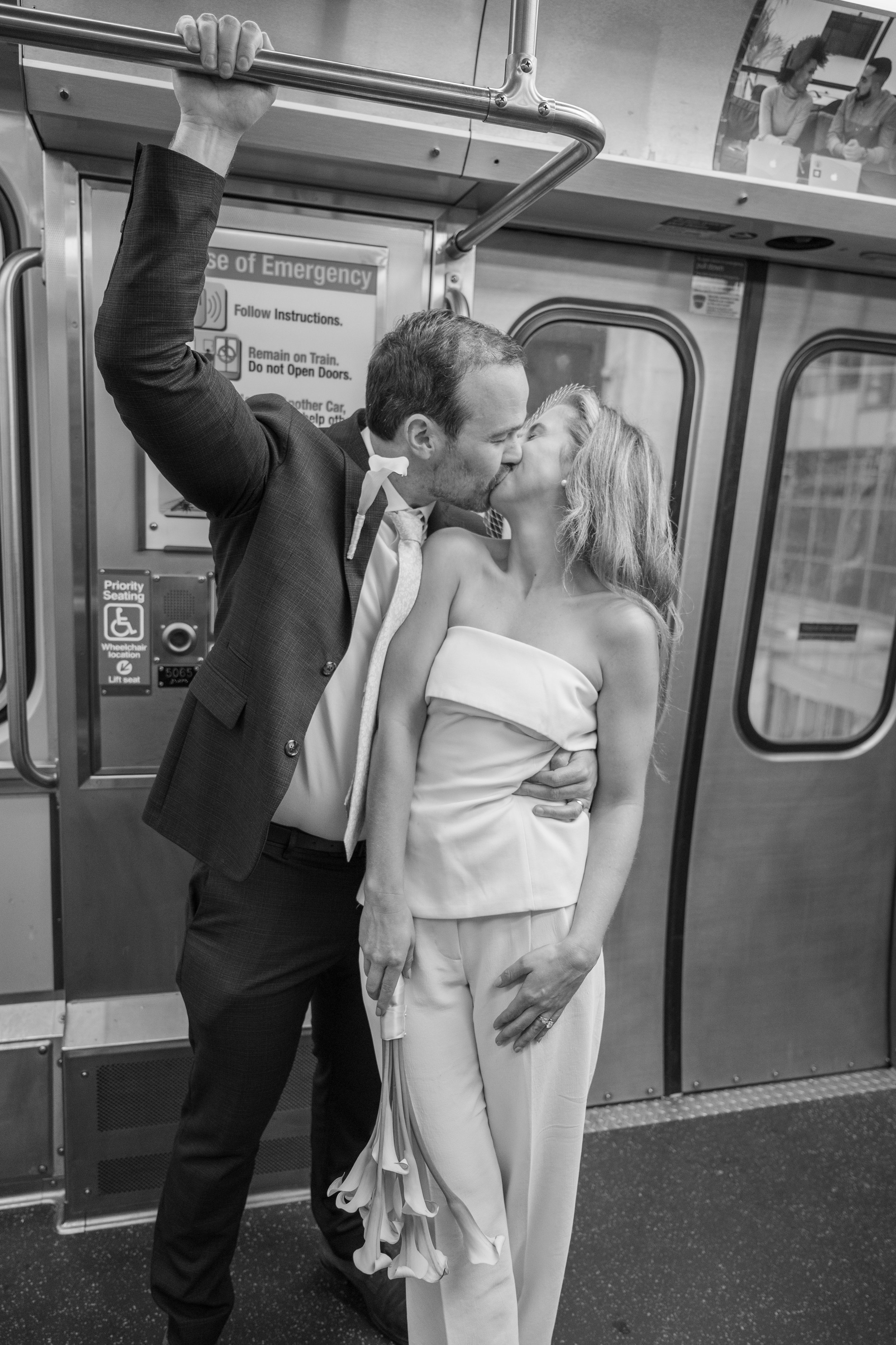 A man and woman share a kiss on a Chicago train, with the man holding onto a handrail above and the woman holding a bouquet of calla lilies. The photograph is in black and white.