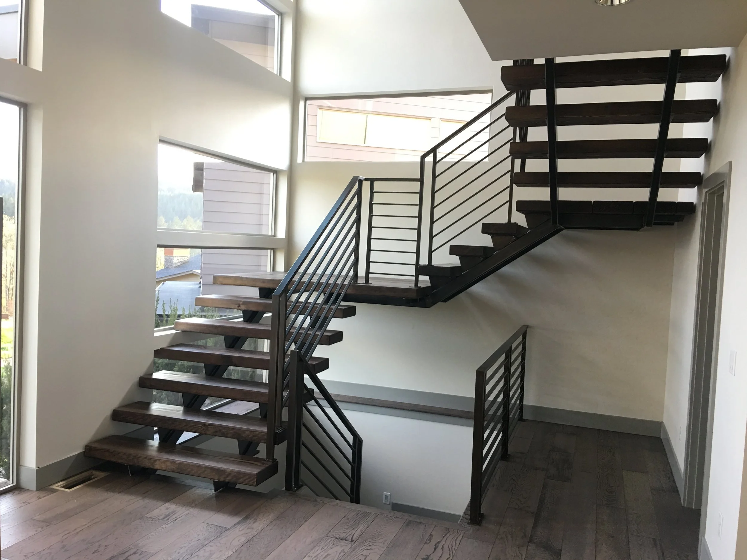 Modern staircase with dark wood steps and black metal railings inside a home, with large windows bringing in natural light.