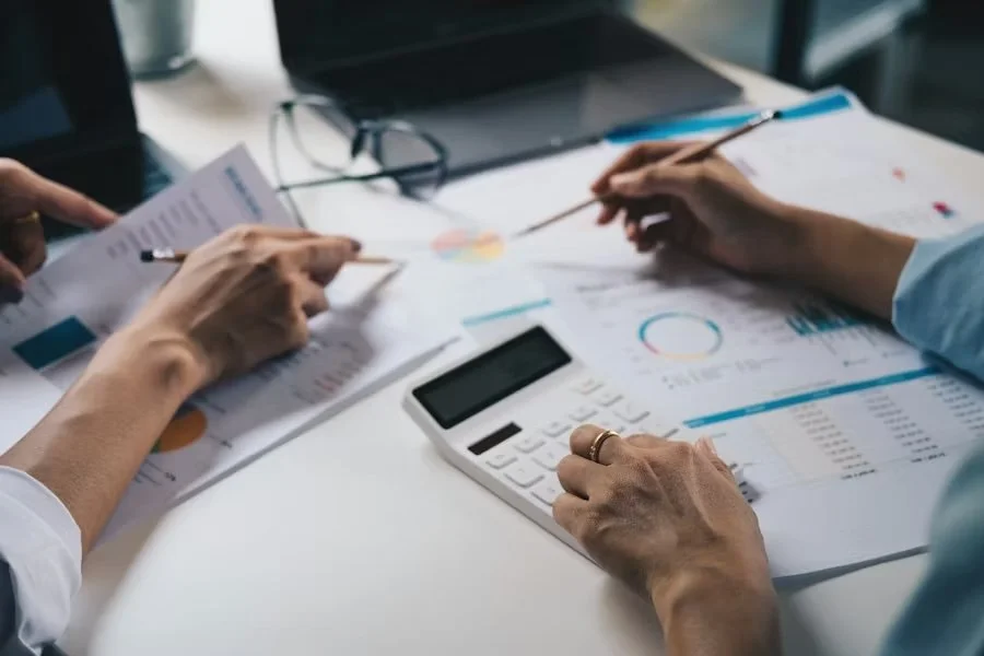 People working on financial documents with charts, a calculator, and pens at a desk.