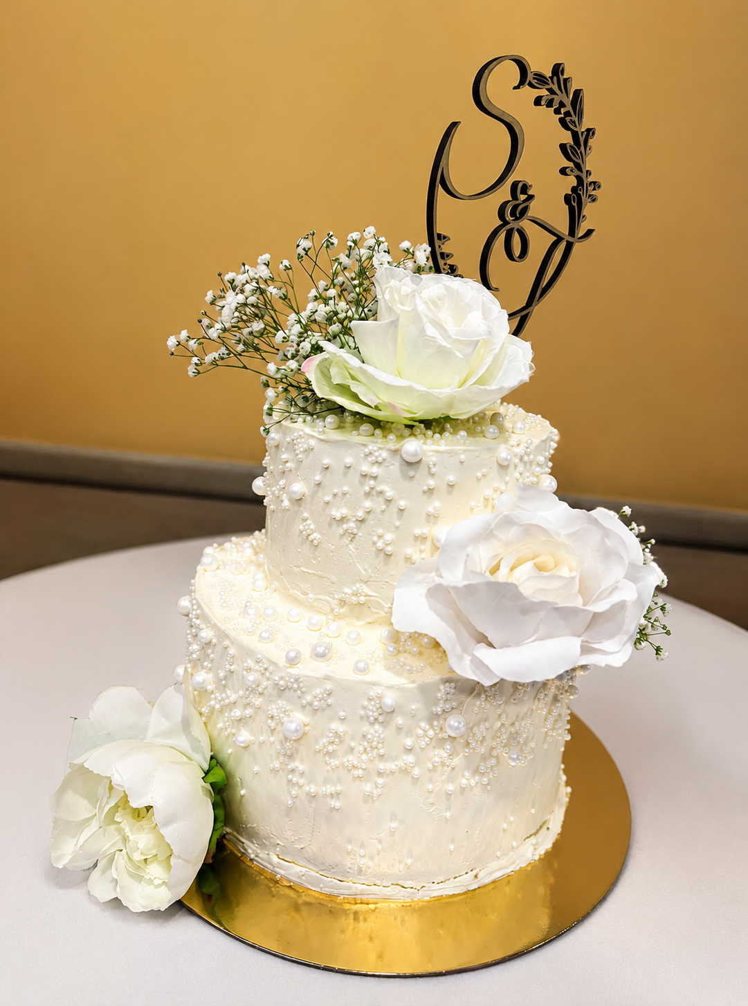 A two-tiered cake decorated with white roses and a cake topper featuring the bride and groom's initials.