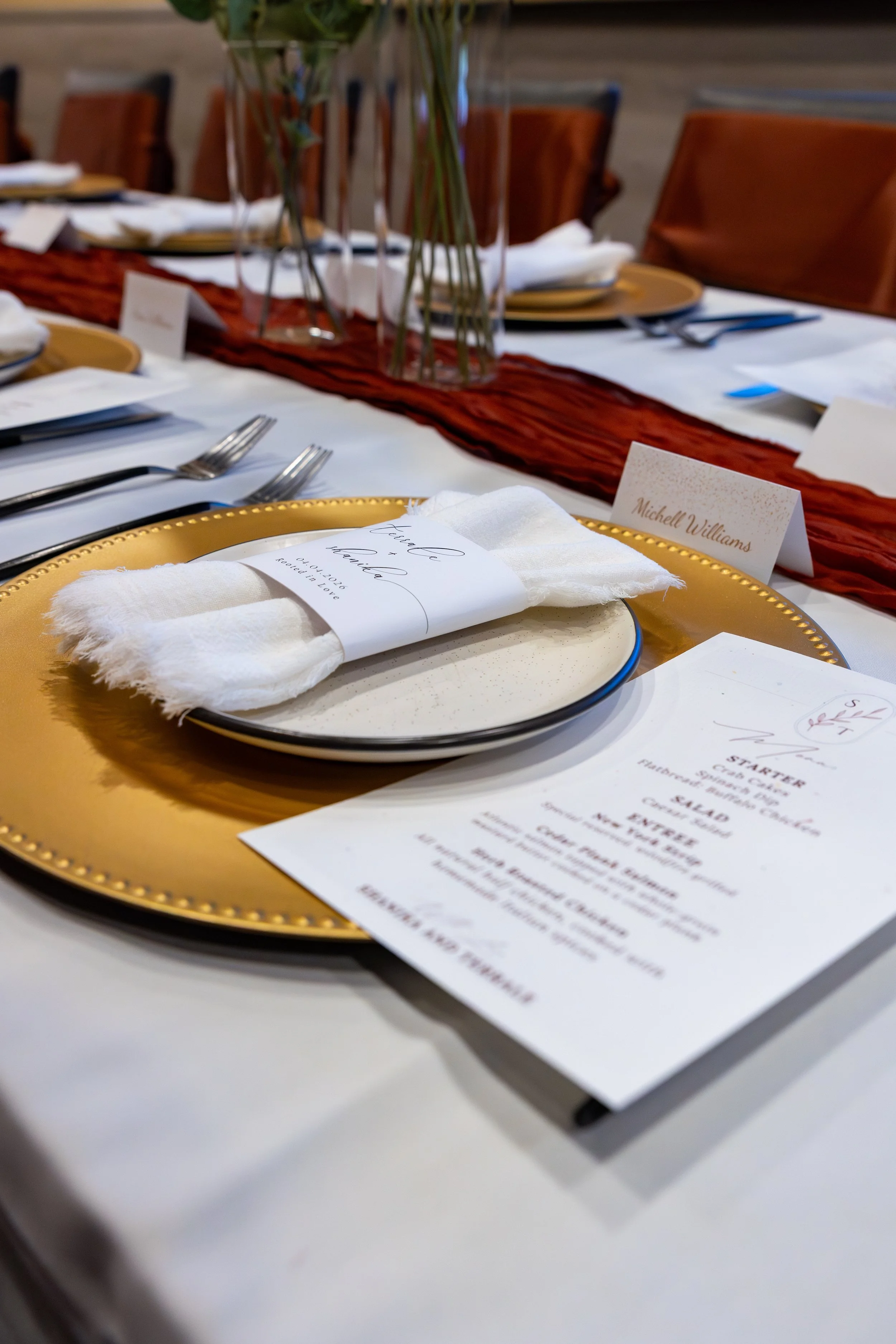 Close-up of a table setting with red details, golden saucers, plates, and a menu.