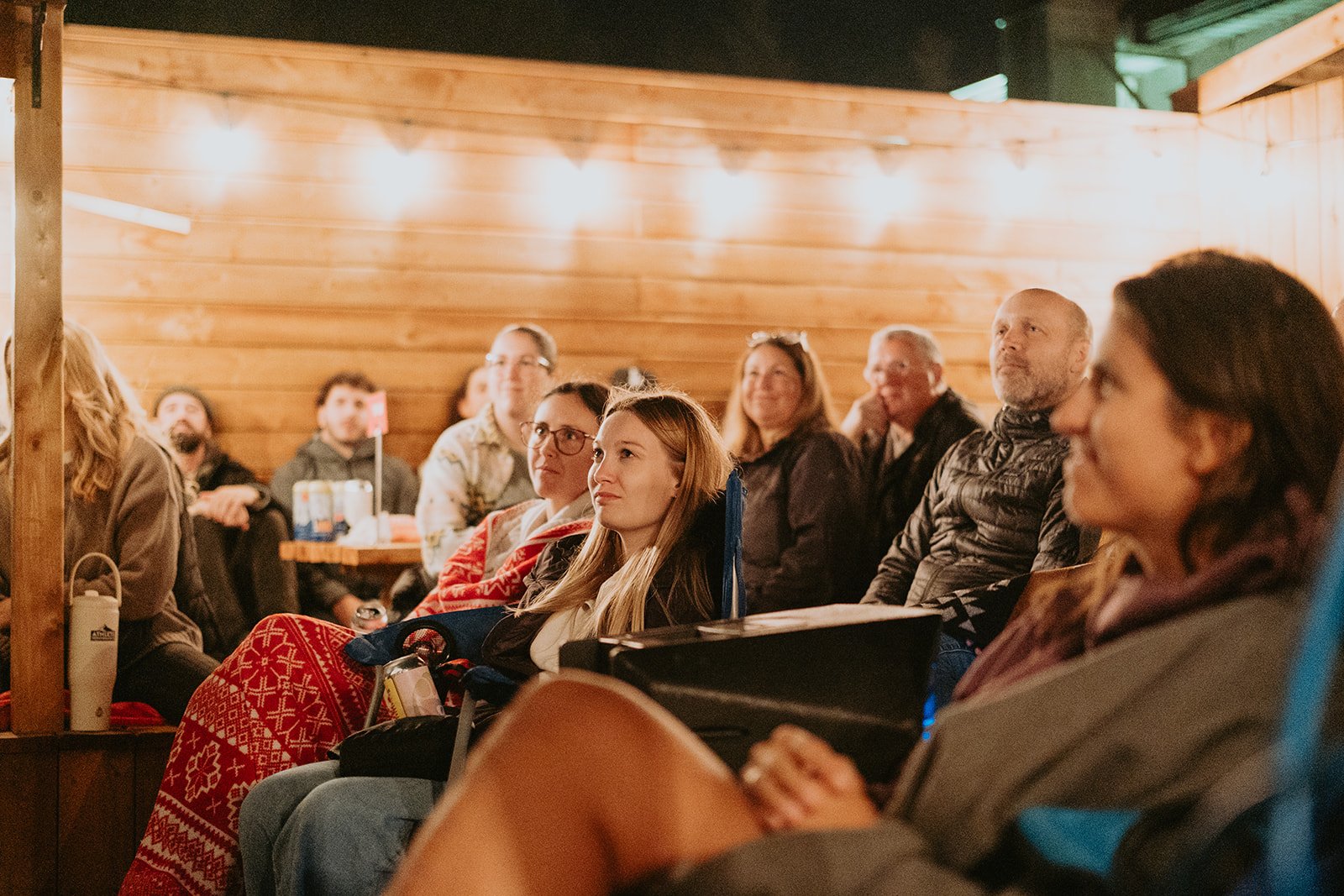Une maison blanche avec un toit en pente noir et des cheminées, entourée d'arbres verts, avec une montagne brumeuse en arrière-plan et un ciel nuageux.