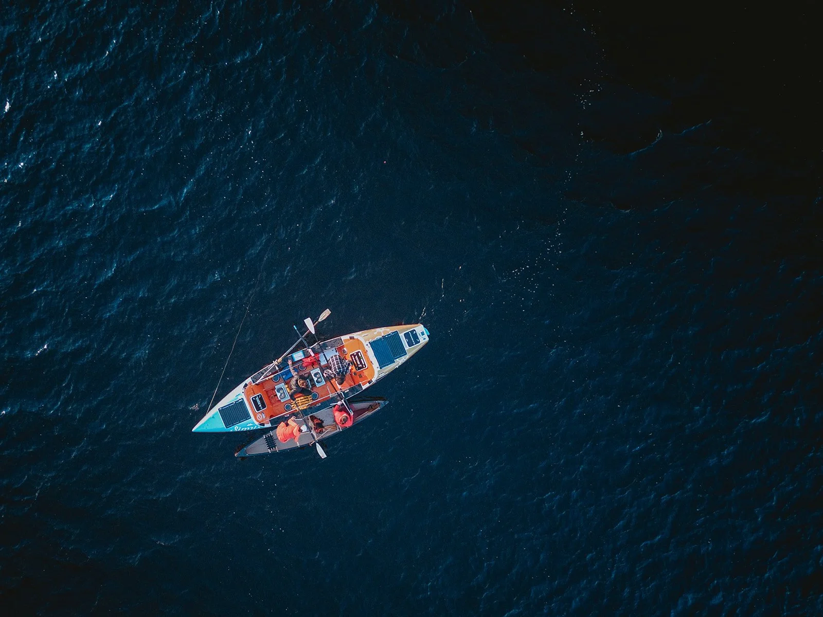 Vue aérienne d'un bateau à rame océanique avec deux personnes à bord, naviguant sur une mer profonde et sombre.