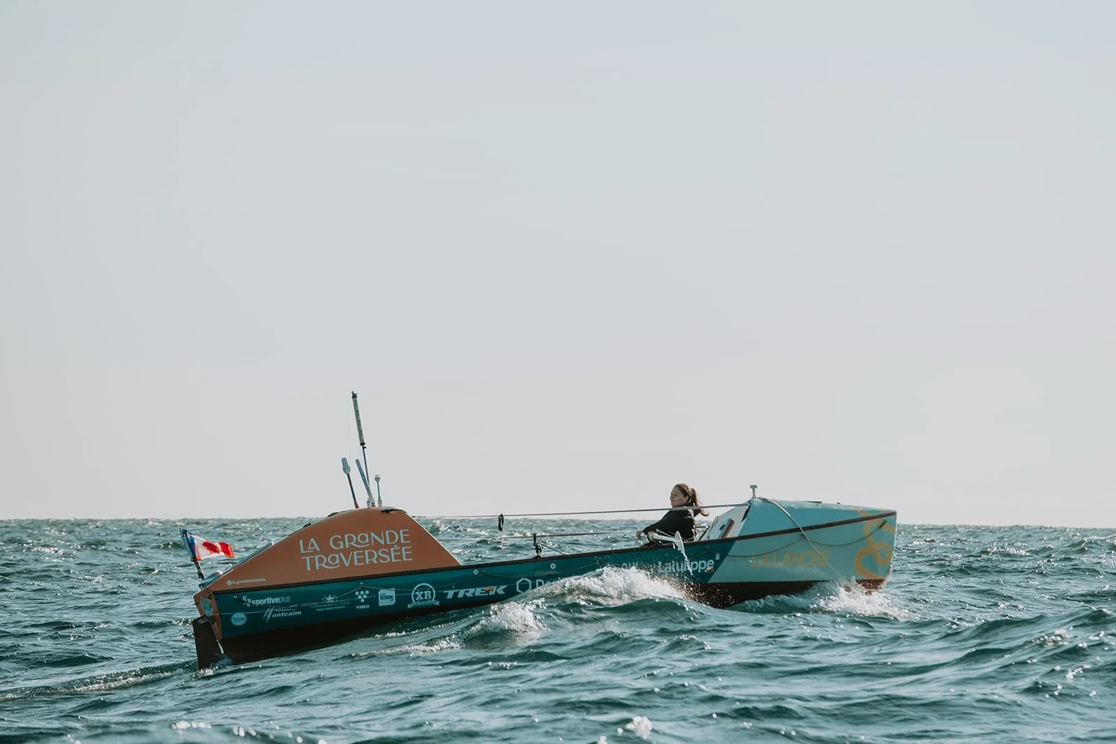 Une femme navigue en voilier sur la mer, le bateau porte les mots 'LA GRANDE TRAVERSEE'.