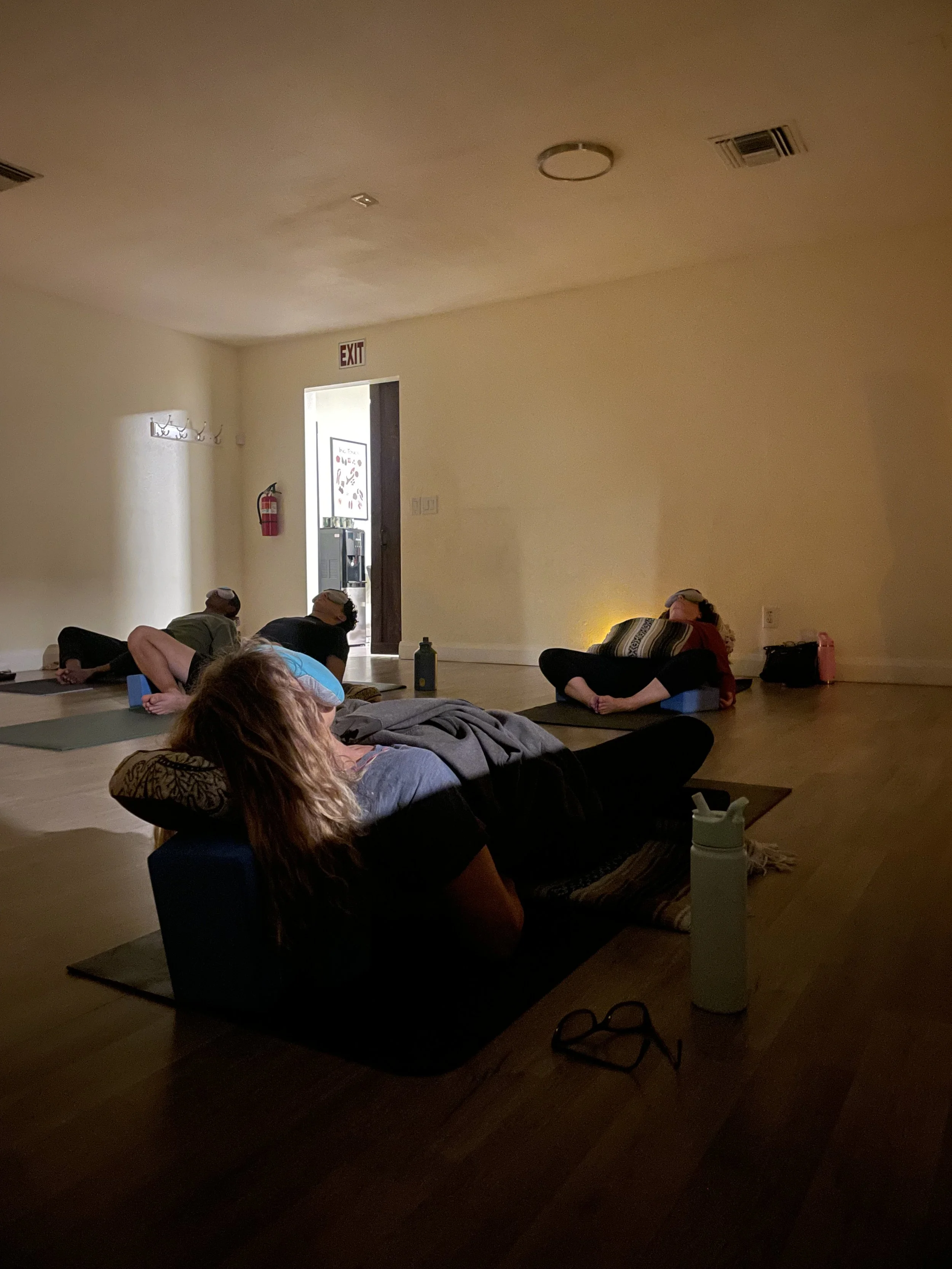 People participating in a yoga or meditation class in a dimly lit room, laying on mats and relaxing.