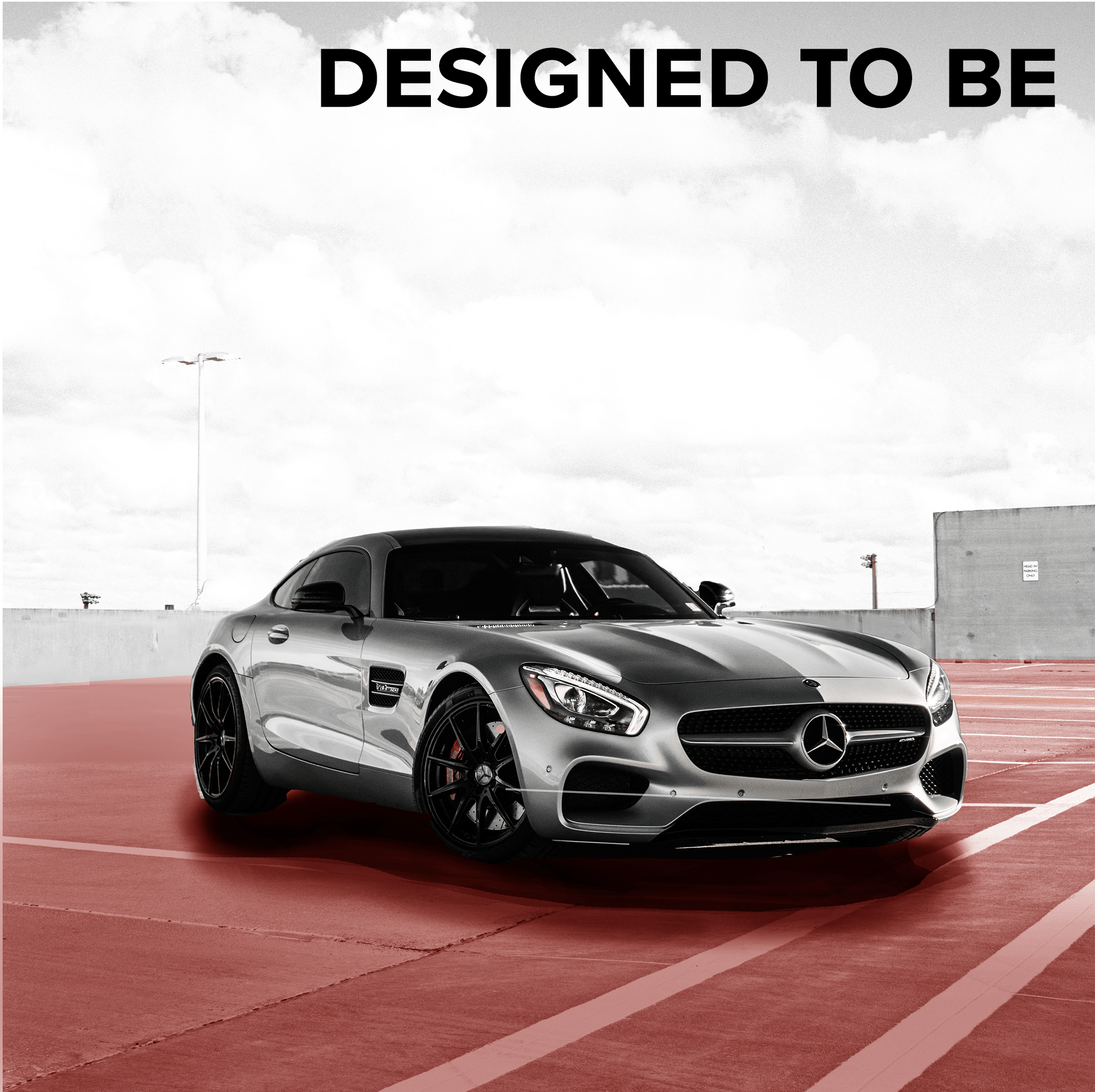 A silver Mercedes-Benz sports car parked on a red parking lot with a mostly clear sky in the background.