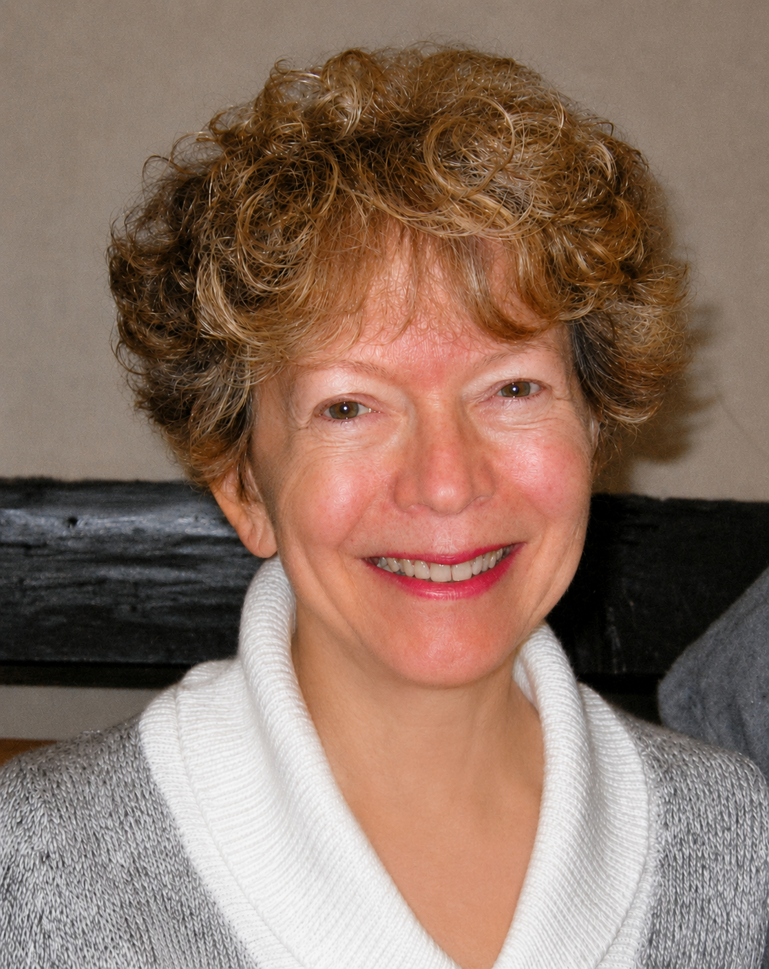 Close-up of Alison, Celebrant, smiling with curly red hair, wearing a white shawl-neck jumper.