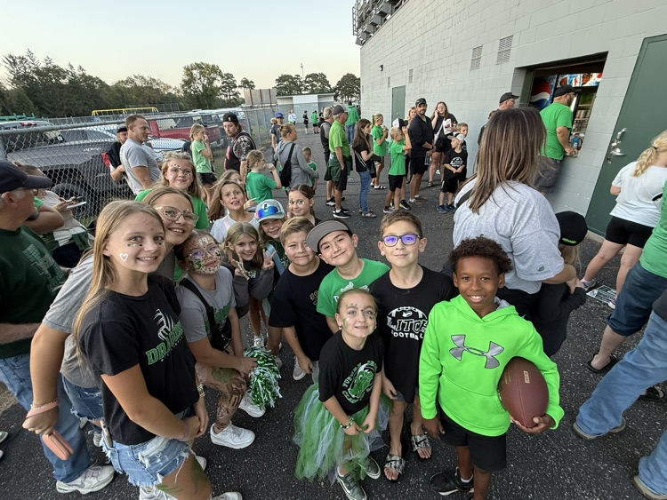 Group of children waiting in line at a ticket booth outside a stadium or event venue, many wearing green and black clothing.