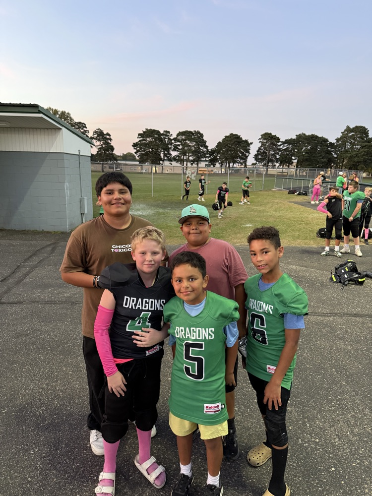 Group of young boys in football uniforms on a field during sunset, with additional players in the background.