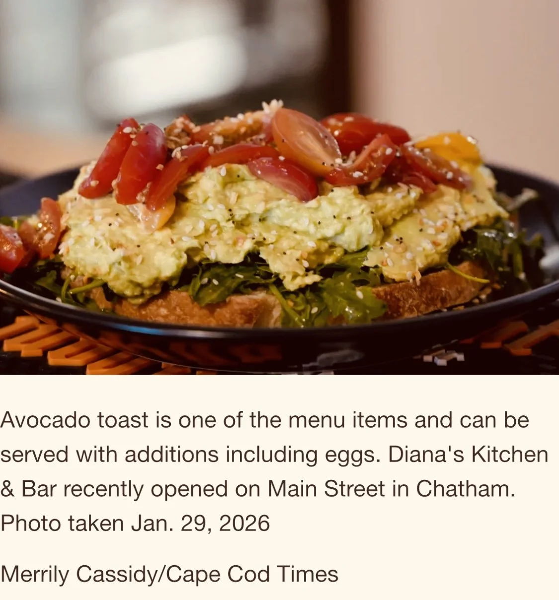 Avocado toast topped with cherry tomatoes and sprinkled with sesame seeds, served on a black plate.